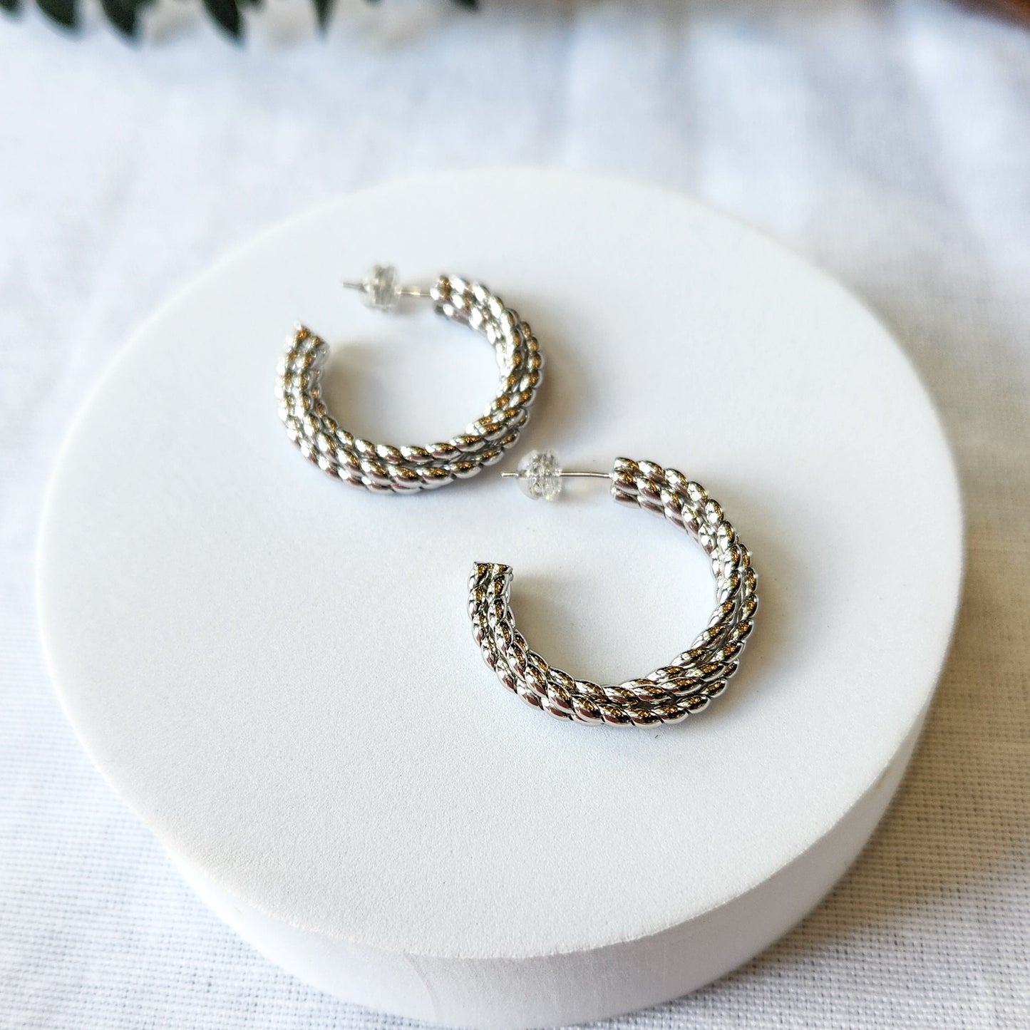 A pair of silver robe hoop earrings with intricate design and small crystal embellishments.