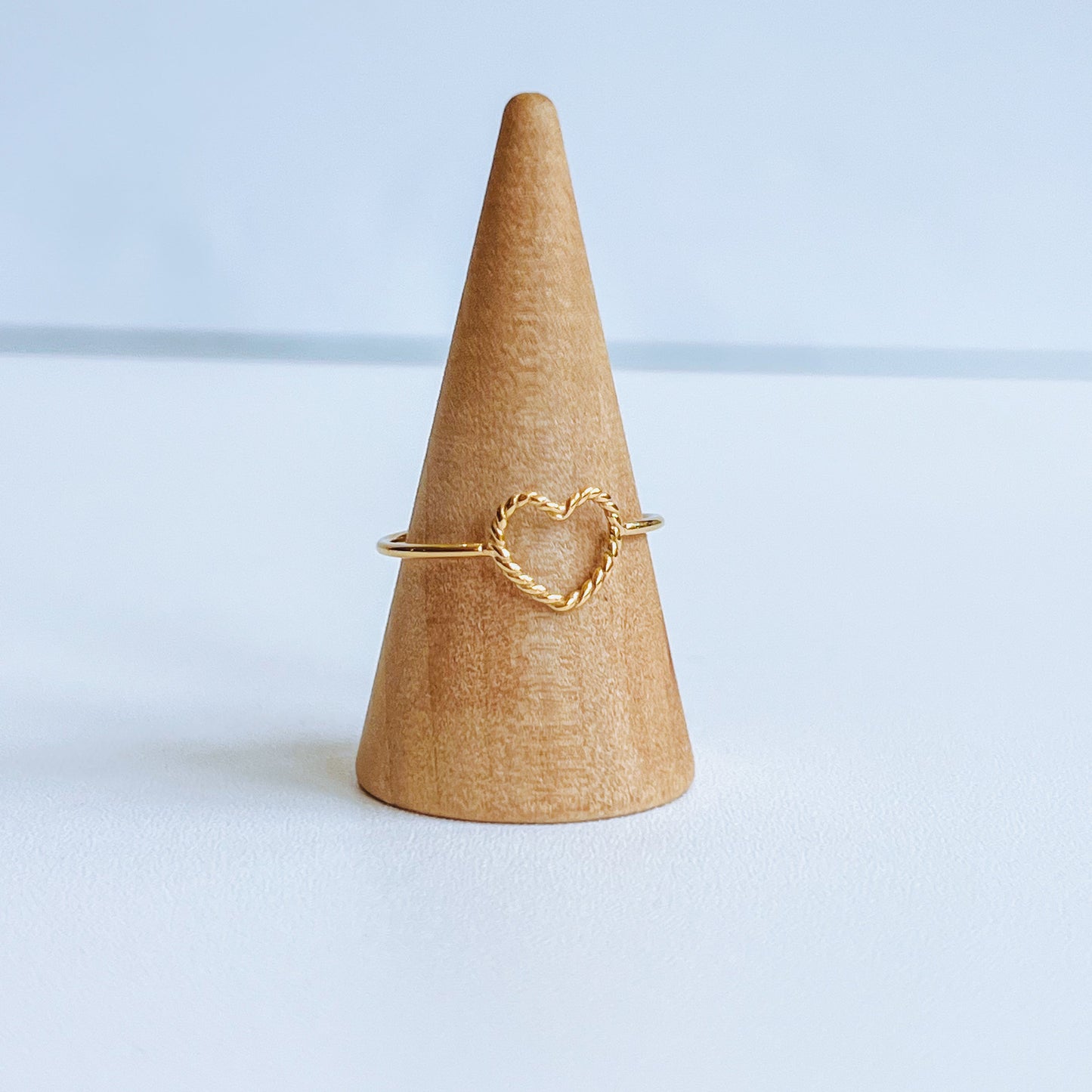 Gold heart-shaped ring on a cardboard cone against a light blue background