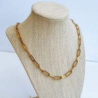 Gold chain necklace on a beige bust against a light blue background