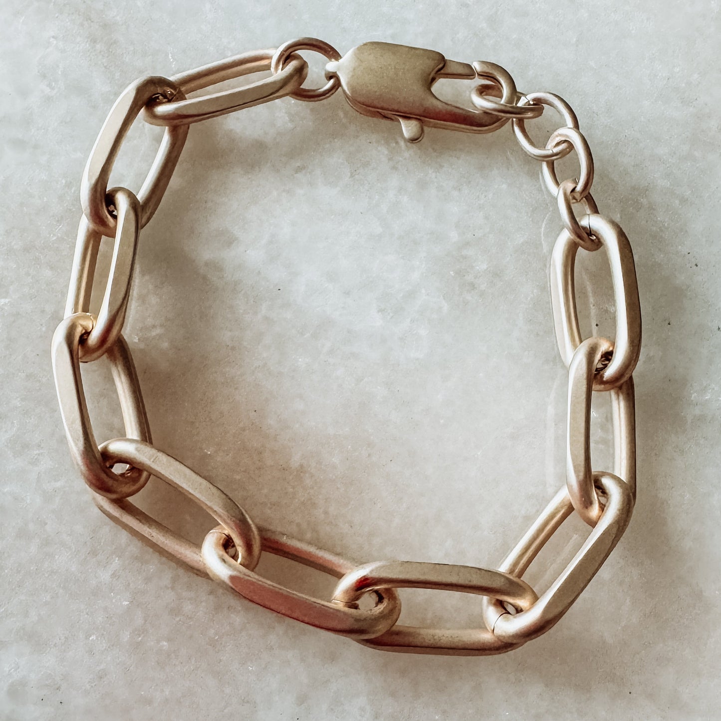 A matte gold bracelet with a chain link design, displayed on a neutral background.