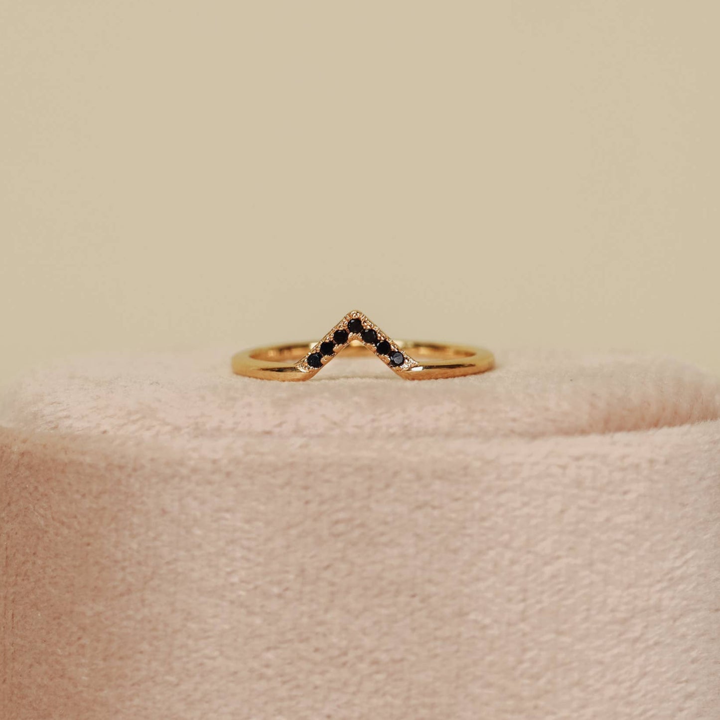 Black Lambda Gold Ring Gold ring with black gemstones on a stand against a beige background