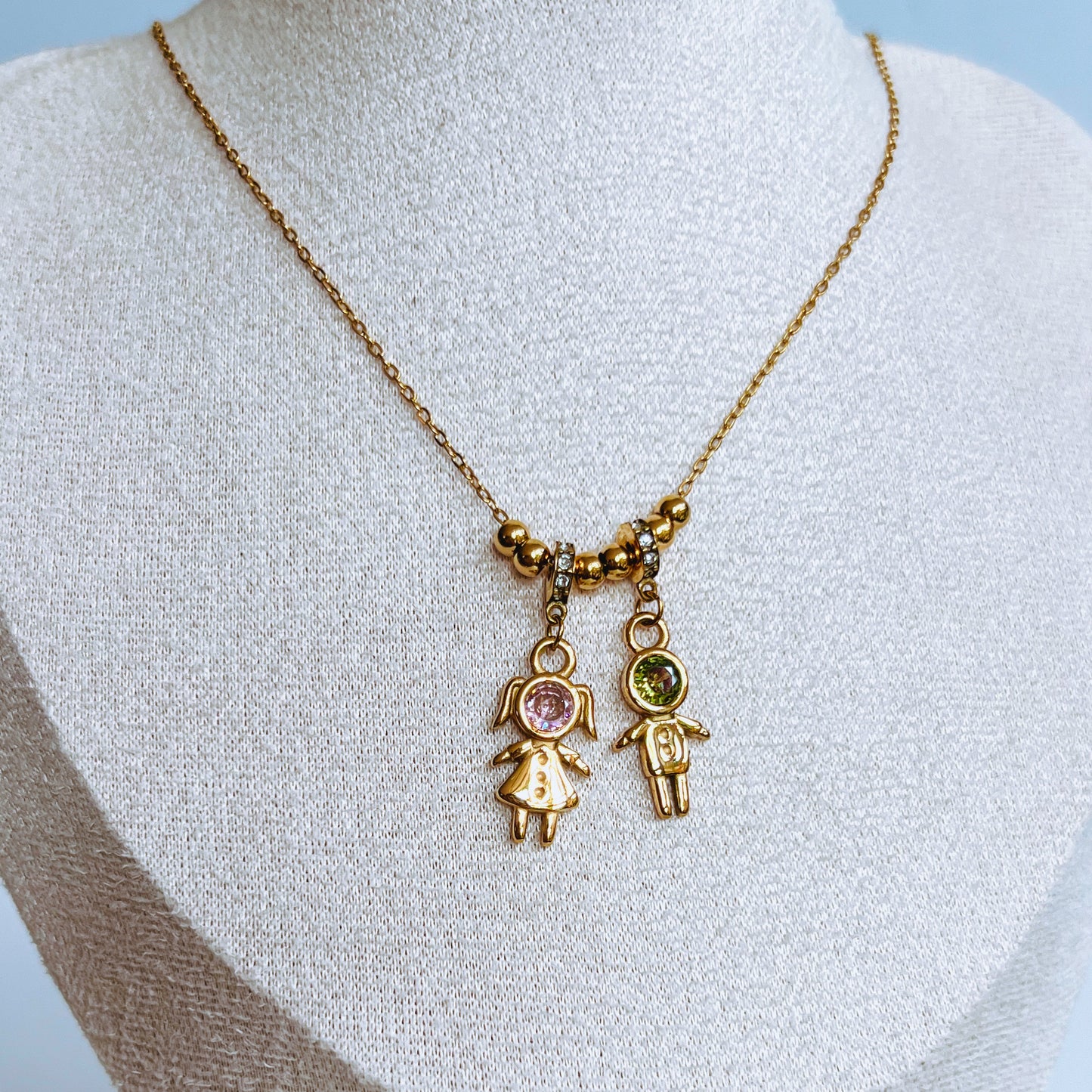 Boy Girl Charm Necklace Gold necklace with two small, decorative pendants on a mannequin bust.