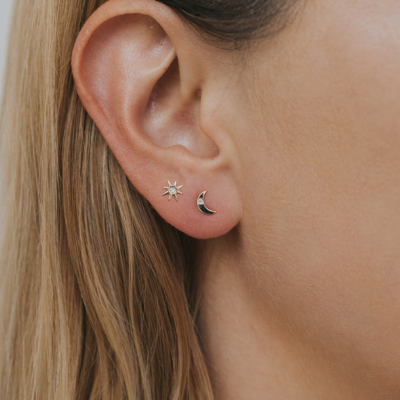 Complements Gold Earrings - Sun & Moon Close-up of a person wearing gold earrings with star and moon designs.