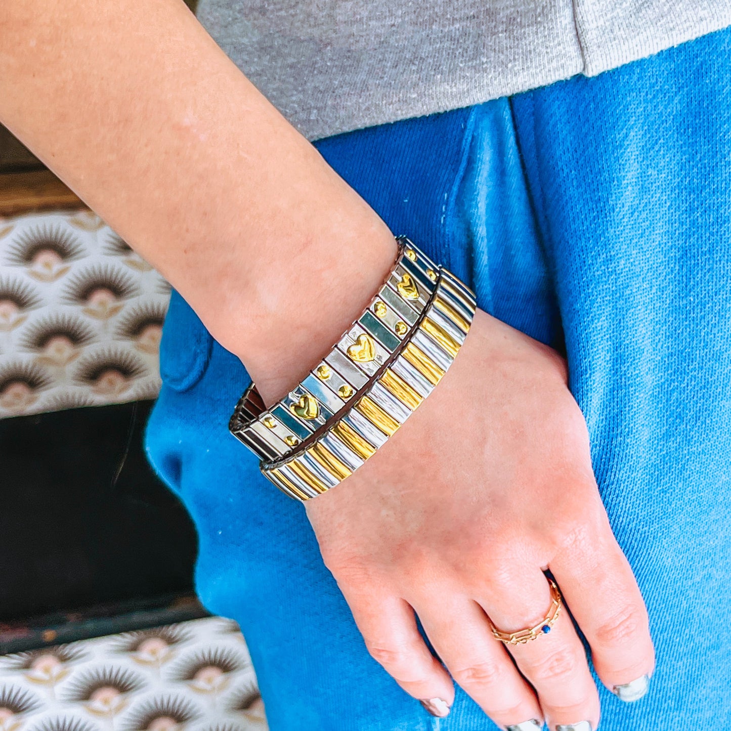 Person wearing a silver and gold bracelets, a Corazón Mixed and Mixed Metal Elastic Bracelet, on a blurred background. 