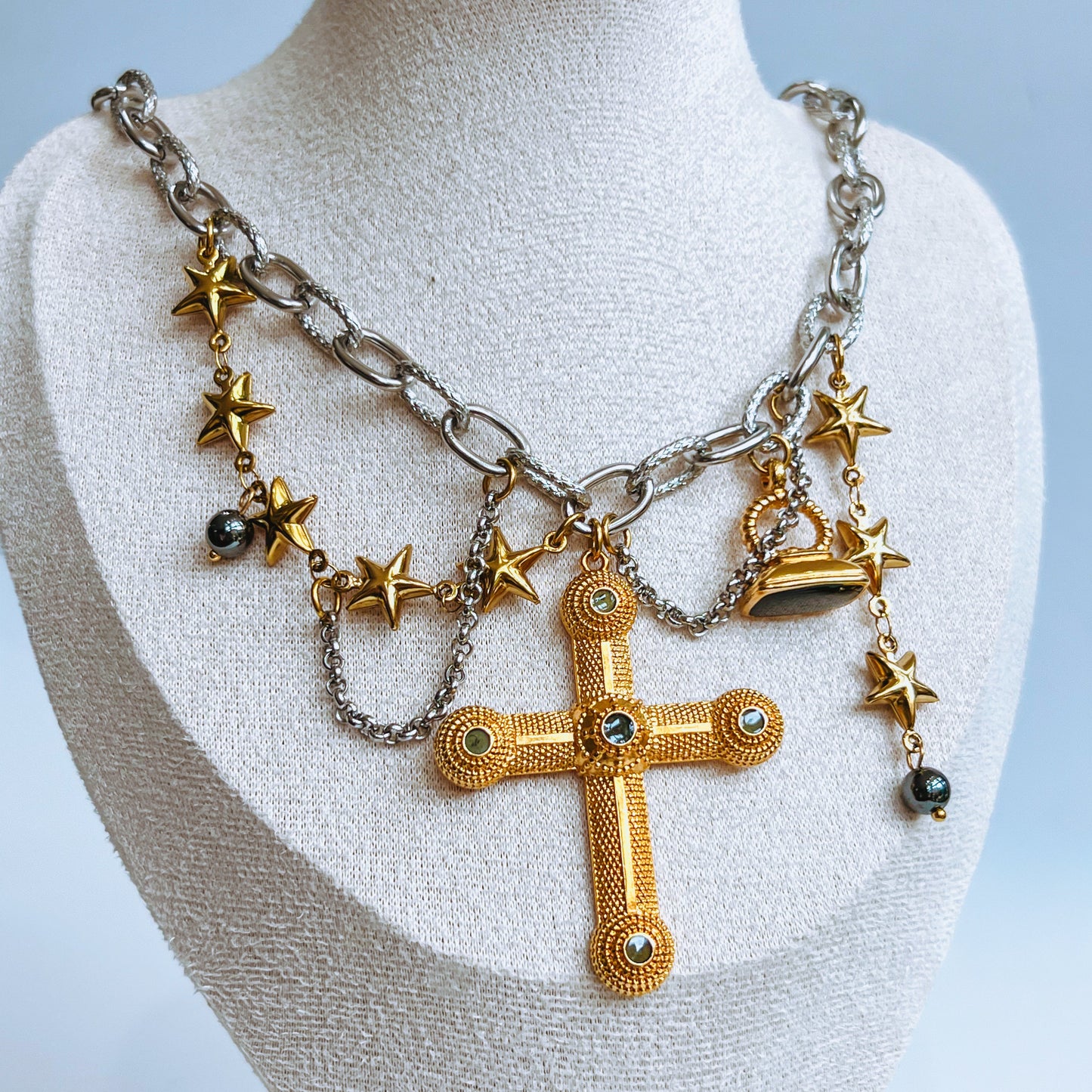 Necklace with gold cross pendant and star charms on a mannequin bust against a light blue background