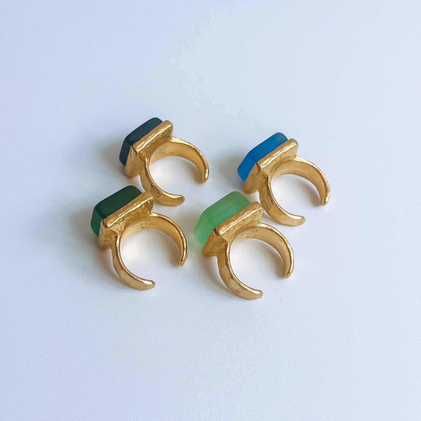 Cube Ring Gold four gold plated open back rings with green and blue glass on a light background