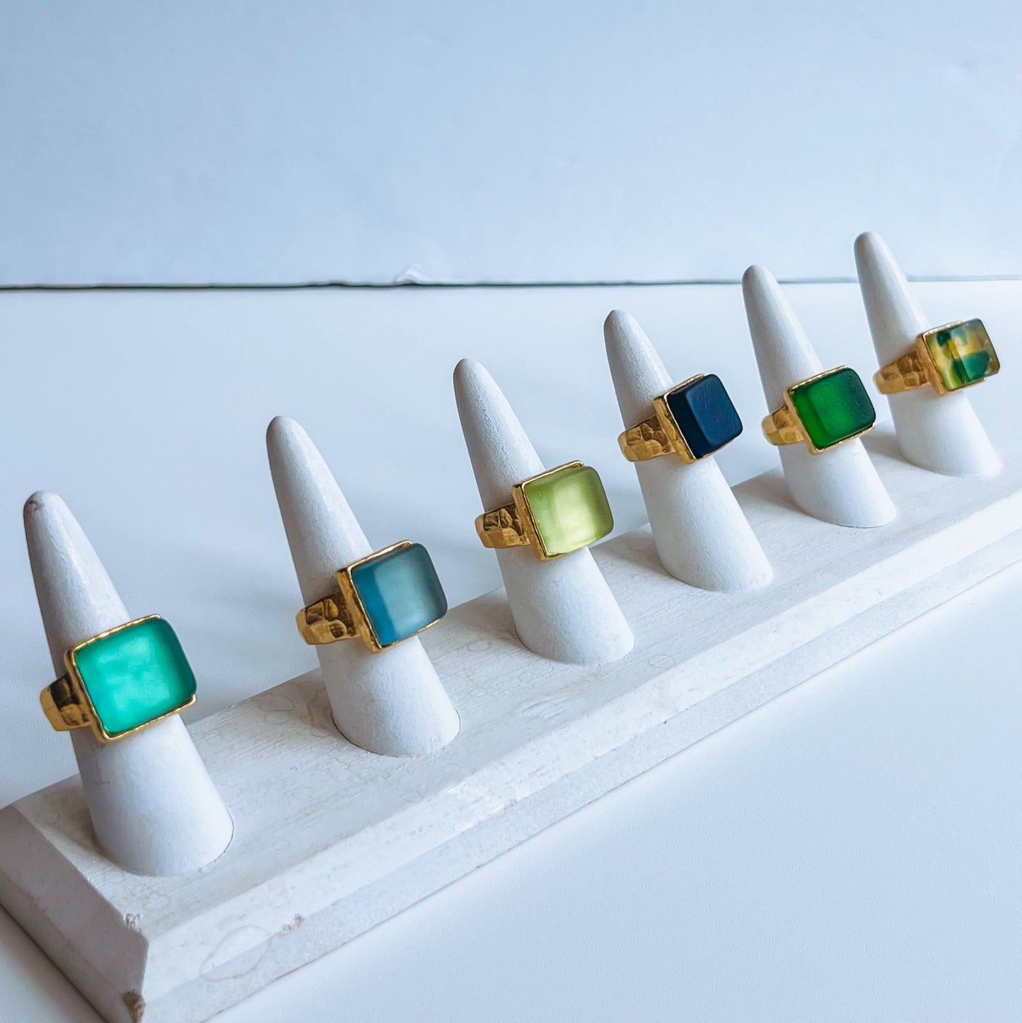 Cube Ring Gold Set of six rings with green and gold accents on ring stands against a light background