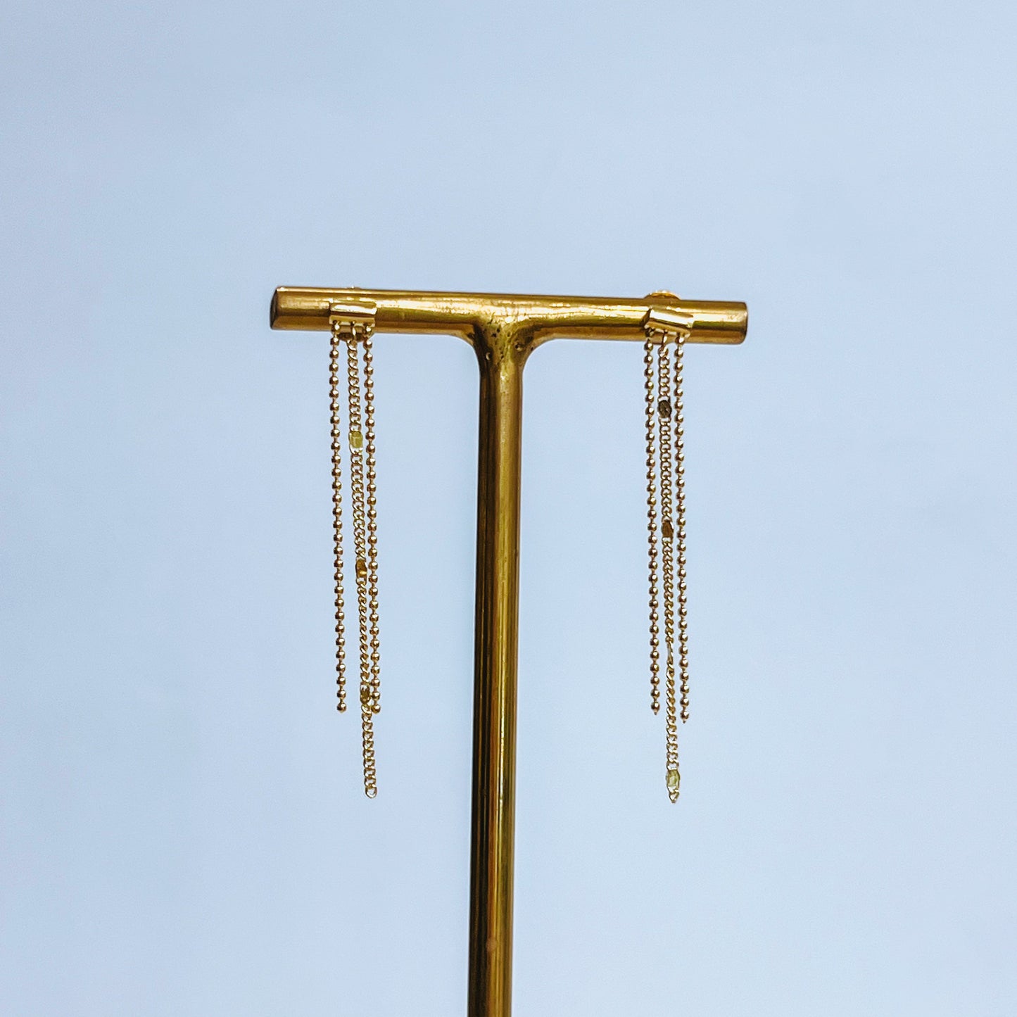 Dainty Gold Chain Earring Gold strand earrings on a gold T-shaped stand against a light background