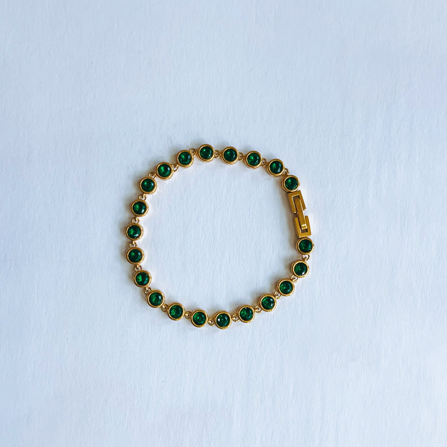 Gold bracelet with green gemstones on a light blue background