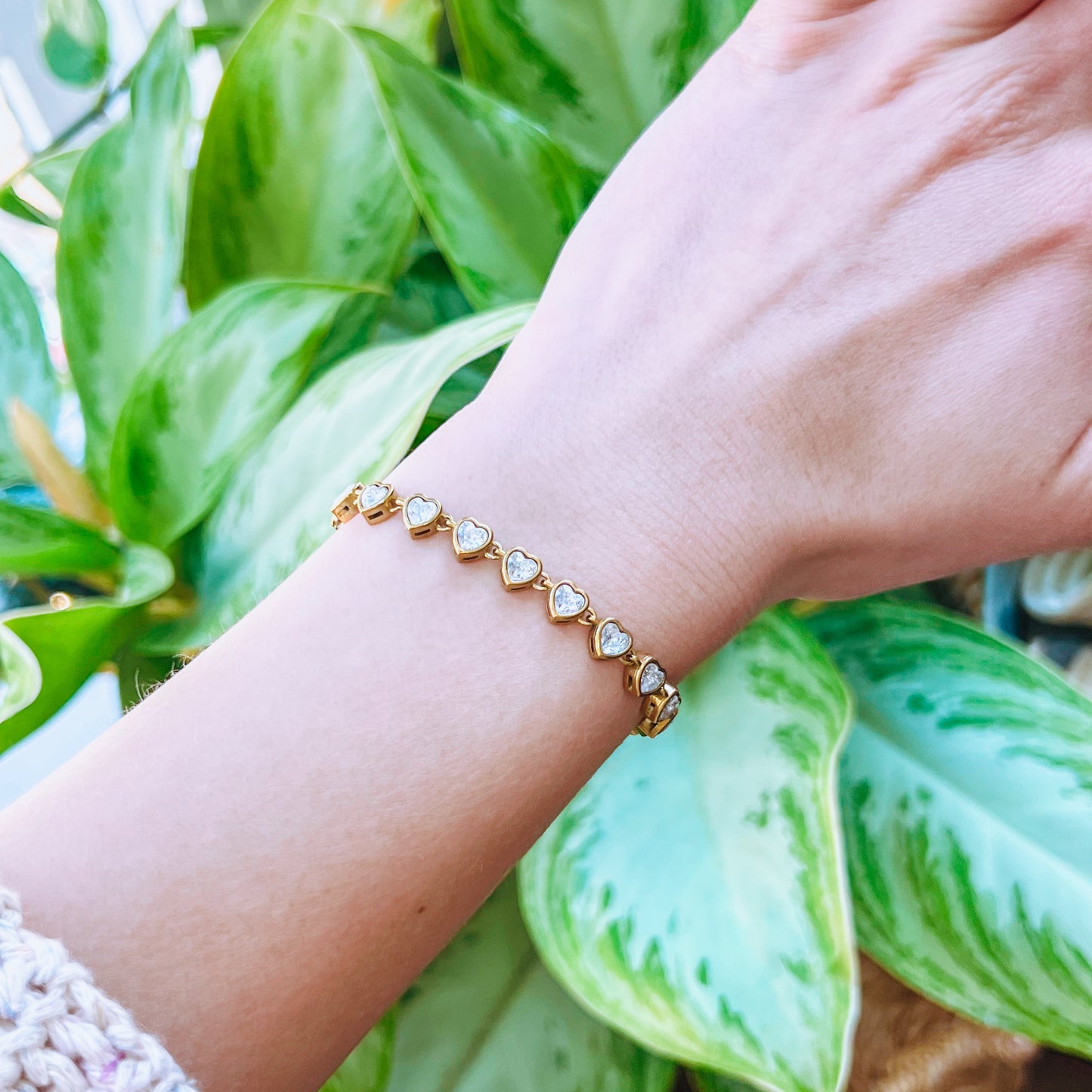 Hand wearing a gold bracelet with green plants in the background