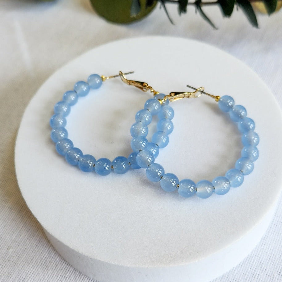 A pair of blue glass bead hoop earrings on a white display stand.