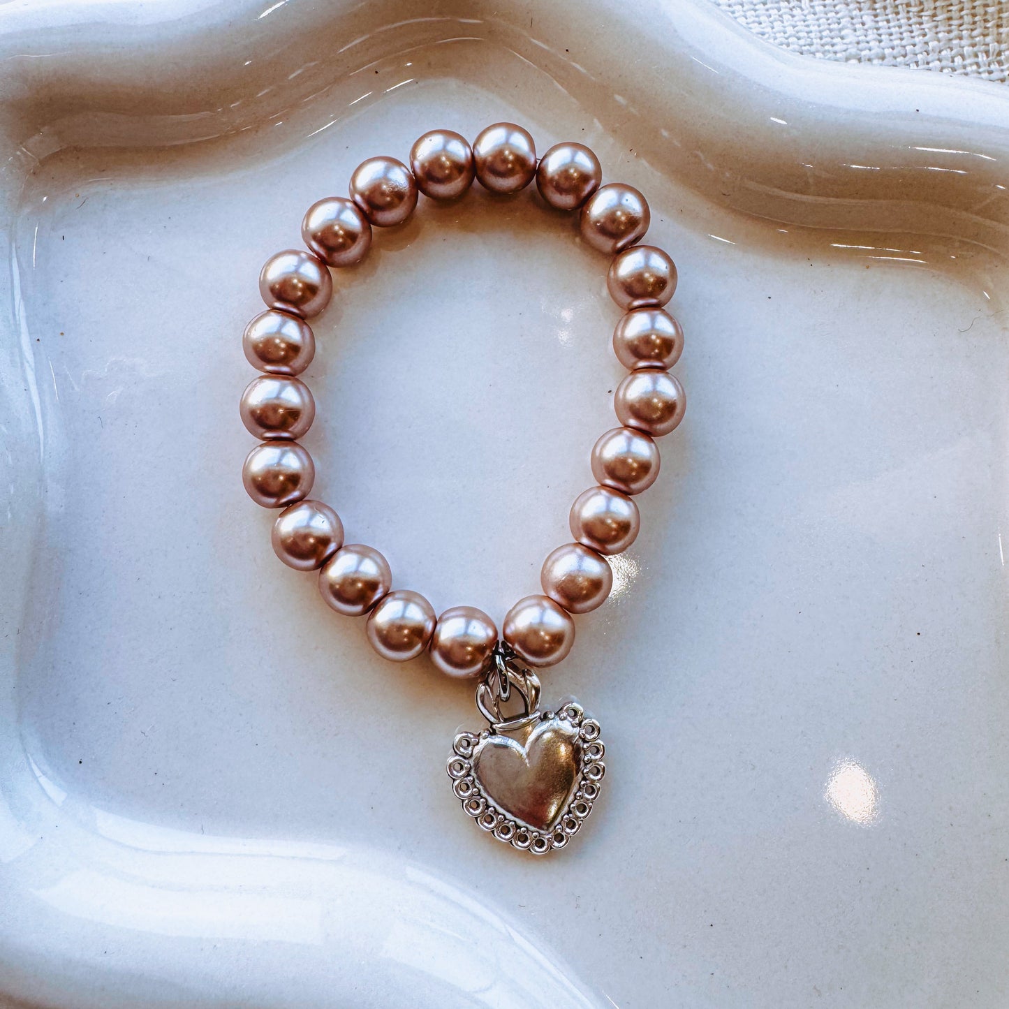 Pearl bracelet with a heart charm on a white background. 