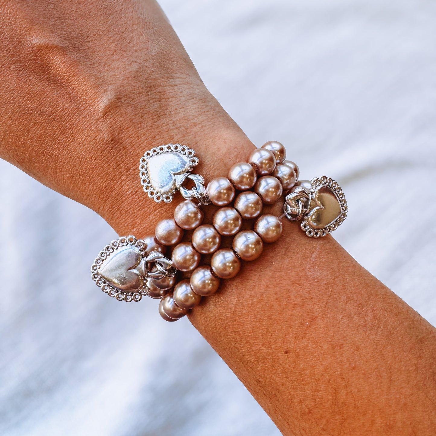 Close-up of a wrist wearing multiple pearl bracelets with heart charms on a blurred background