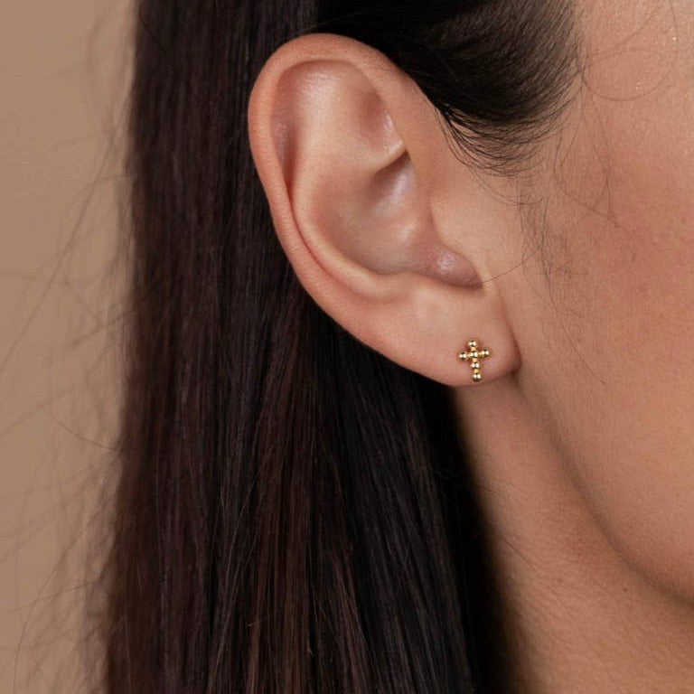 Gold Cross Stud Earrings Close-up of an ear wearing a gold cross earring with a neutral background