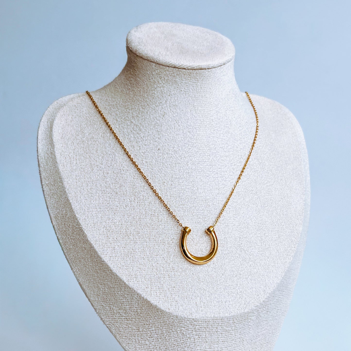 Gold Horseshoe Necklace Gold necklace with a gold horseshoe pendant on a mannequin bust against a light background