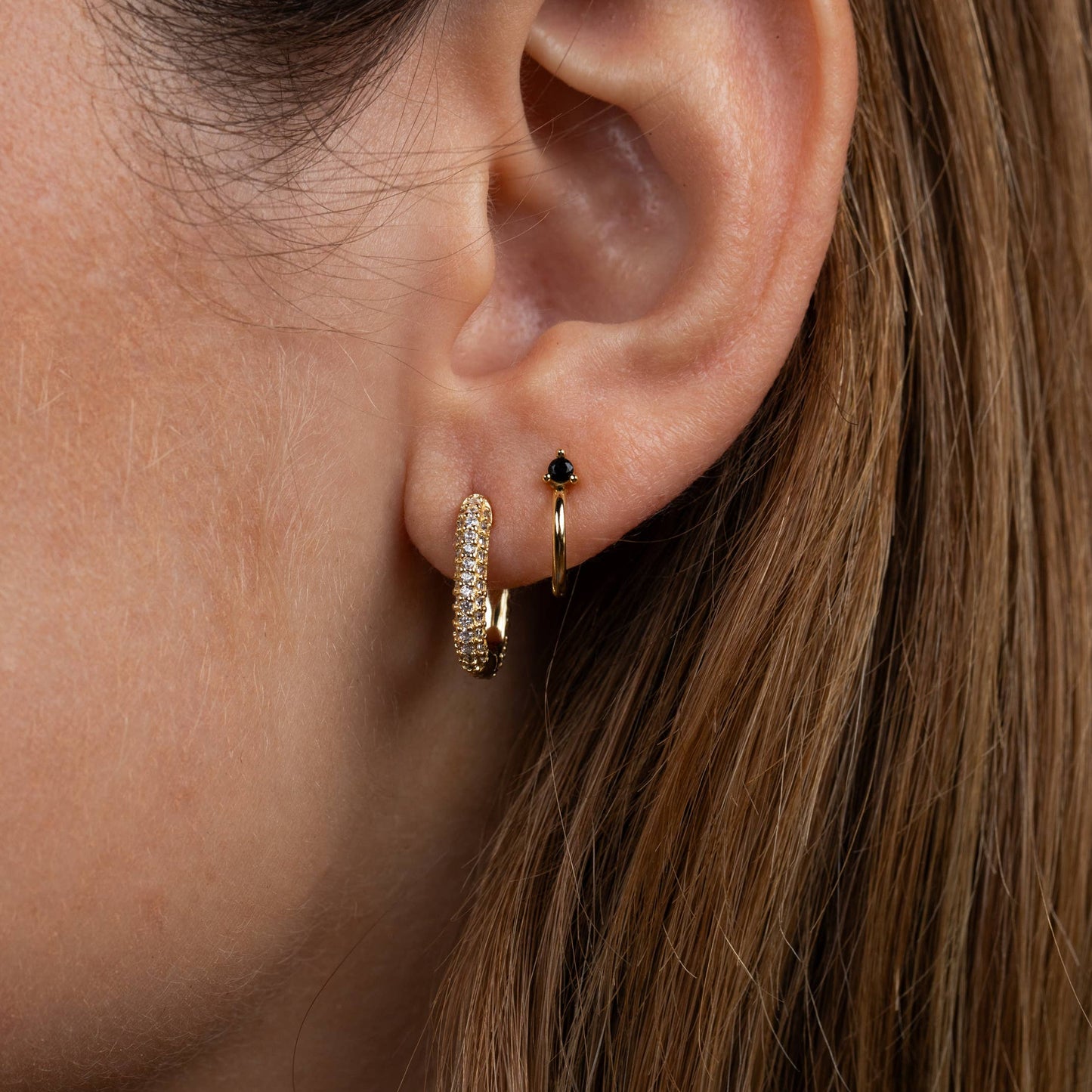 Gold Mini Hoop Earrings - Black Close-up of an ear wearing two different gold hoop earrings 