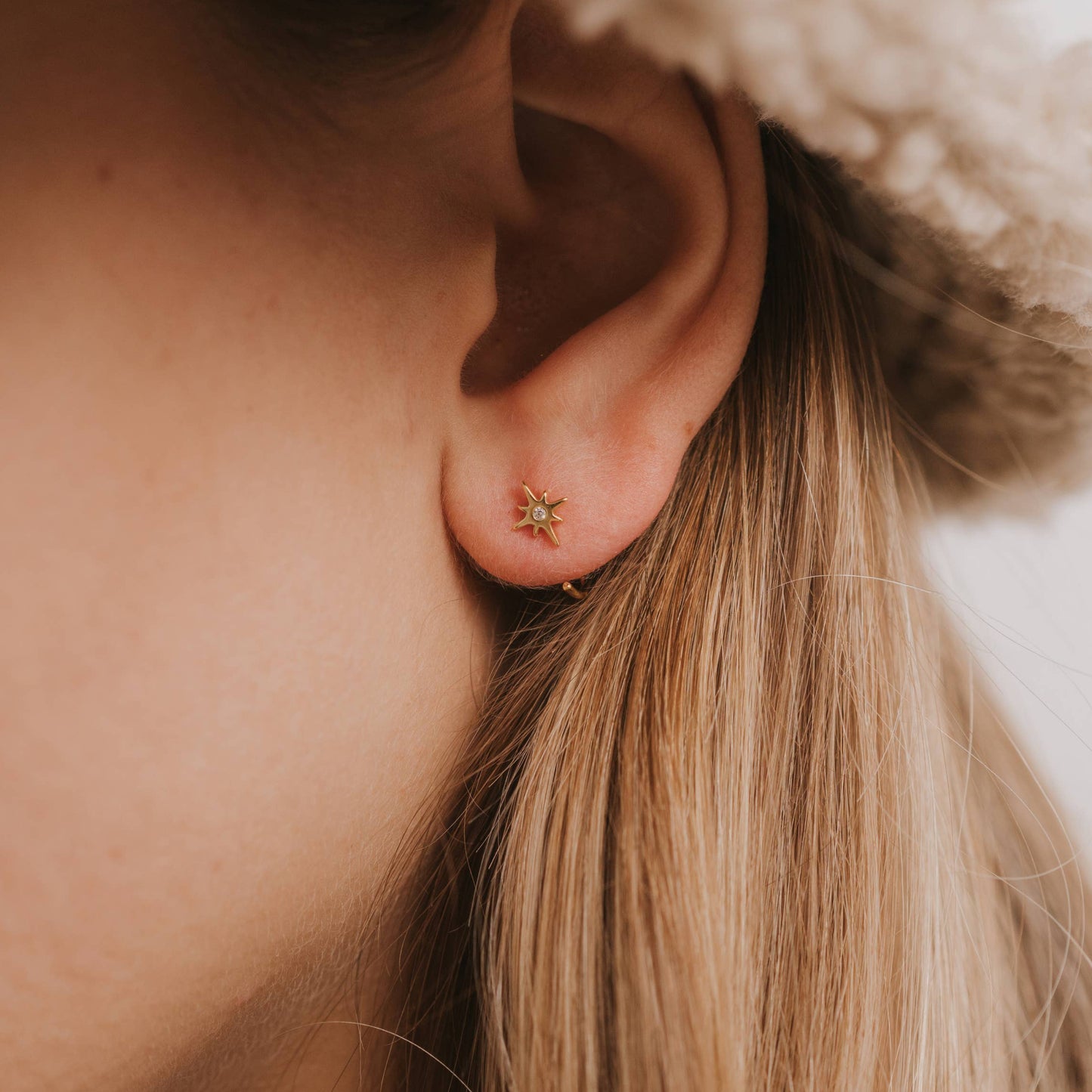 Gold Star Huggies Earrings Close-up of an ear wearing a gold star huggie earring with a blurred background