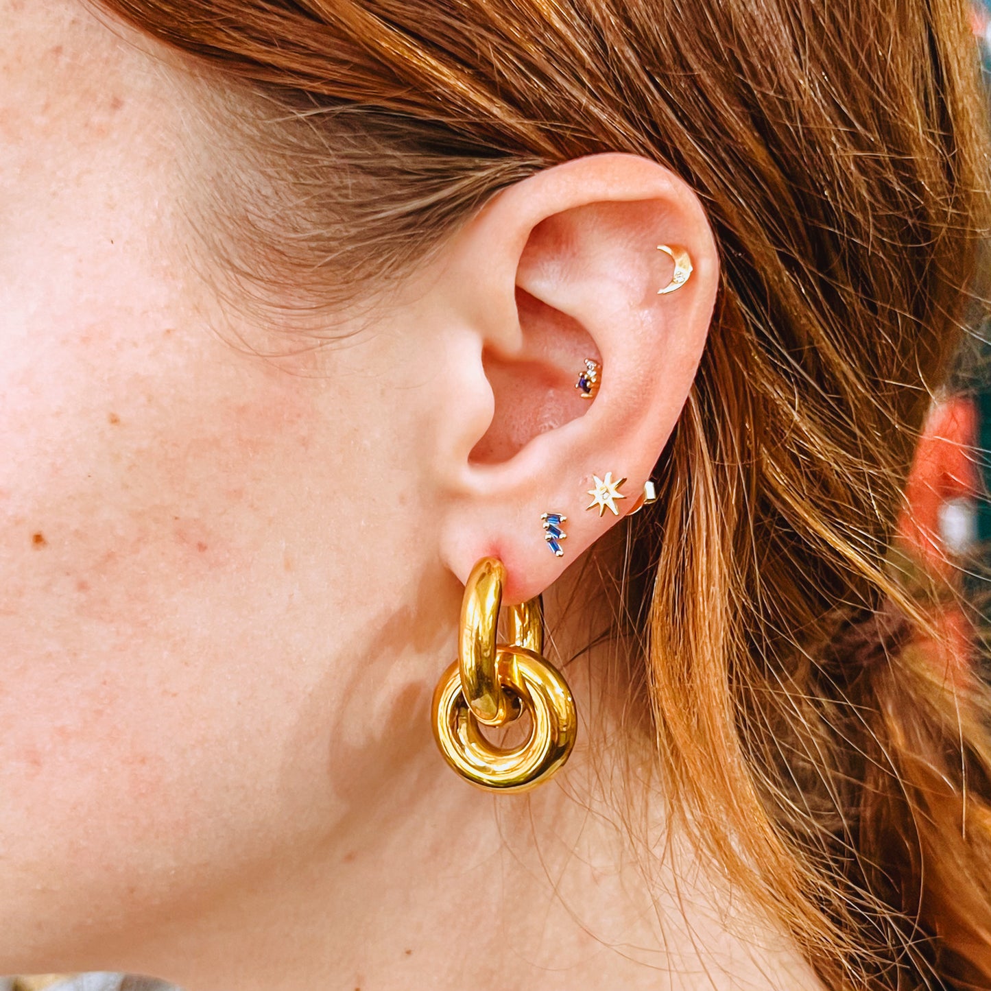 Close-up of an ear with Gold double ring earrings and small star-shaped earrings.