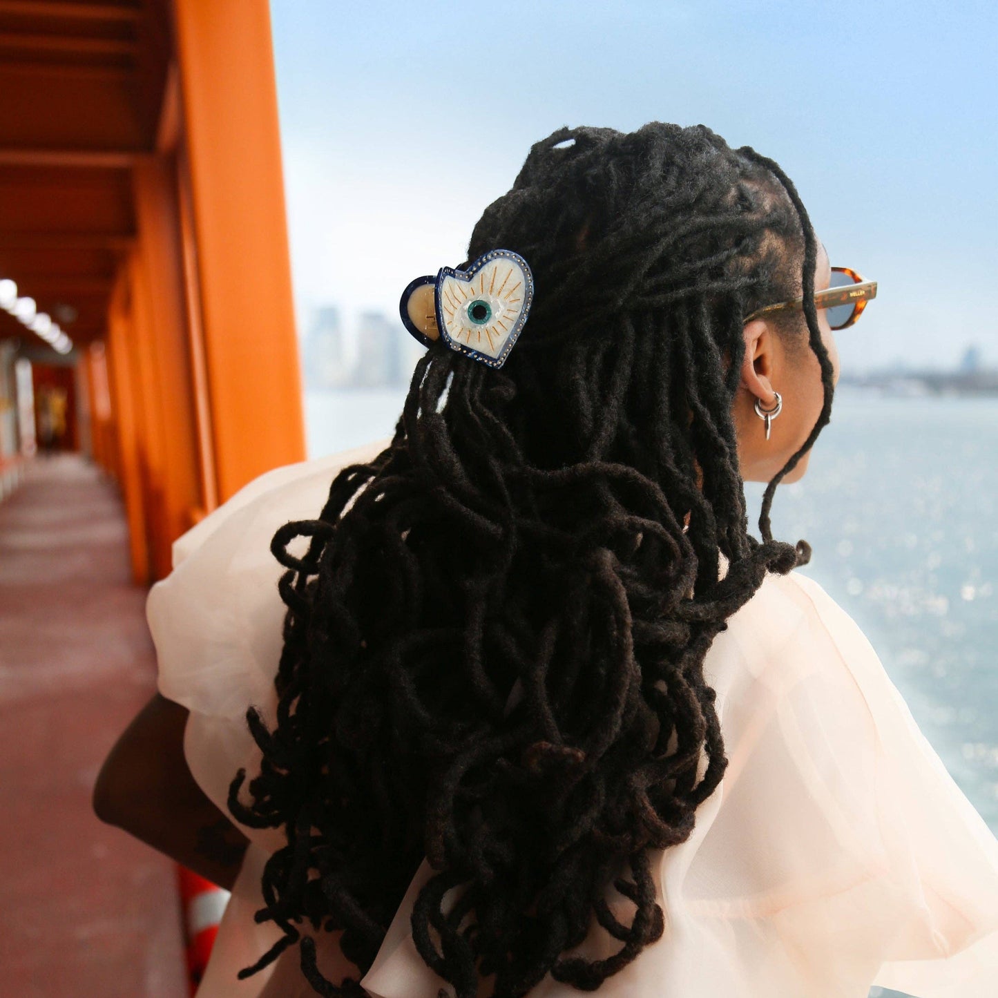 Person with styled hand-painted hair clip in hair by a waterfront. 