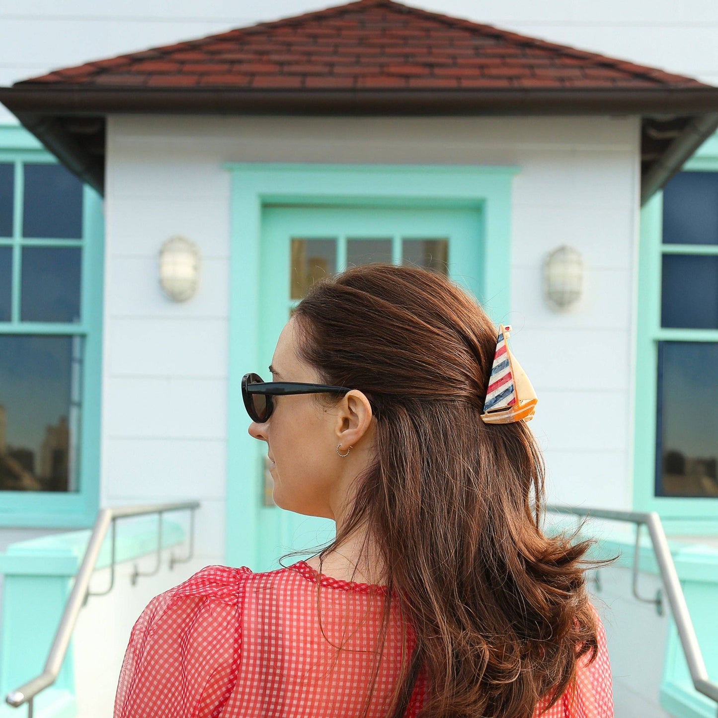 Woman in a red dress with a colorful Hand-painted Sailboat Claw Hair Clip standing in front of a building with a turquoise door.