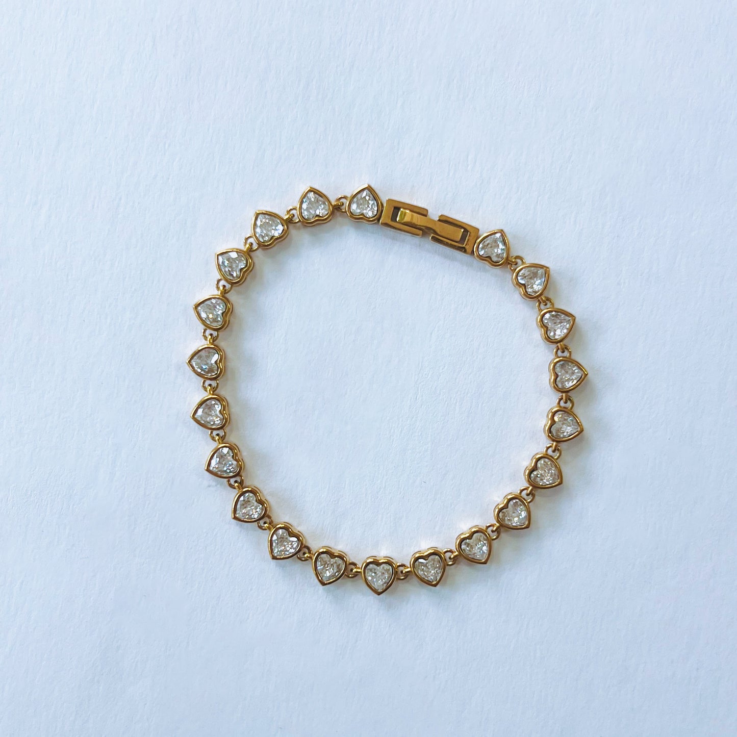 Gold bracelet with heart-shaped diamond stones on a light blue background