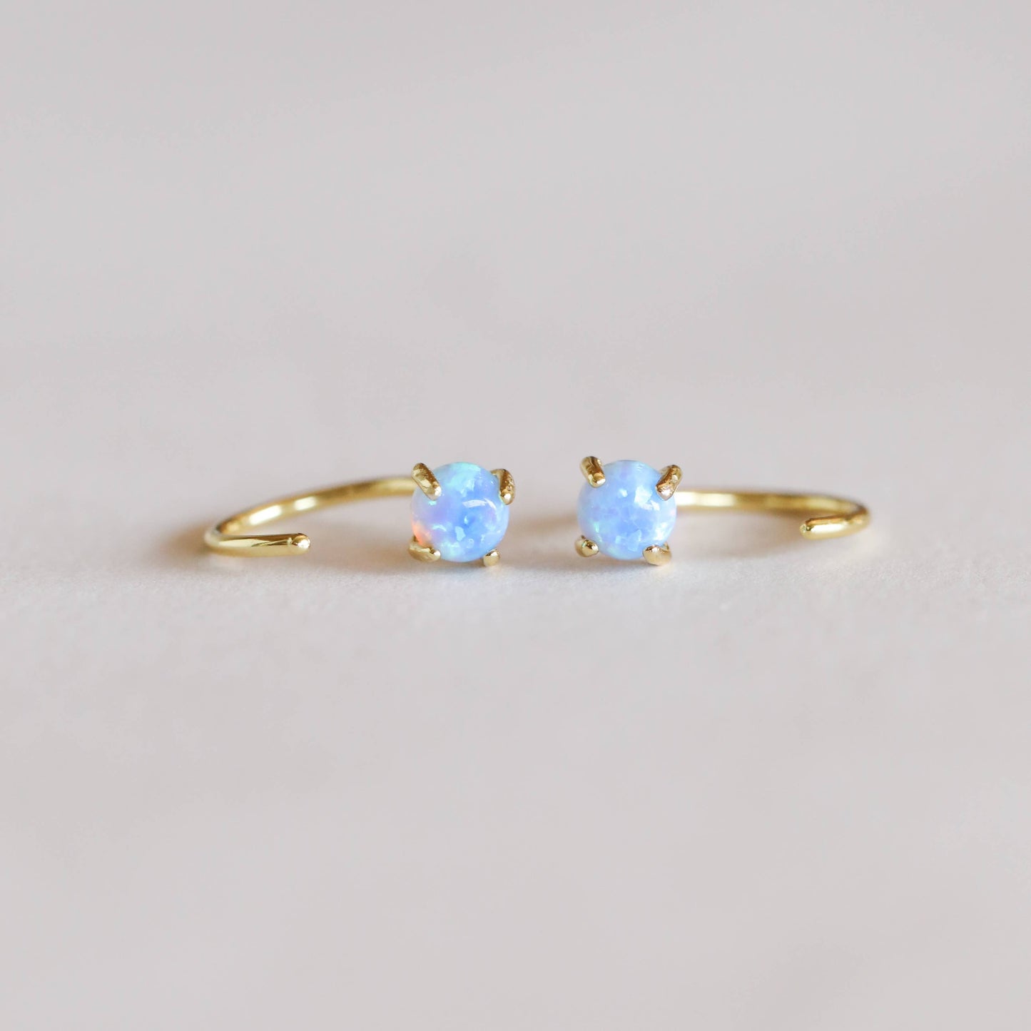 Huggies Gold Earrings - Fire Opal Pair of gold hoop earrings with blue gemstones on a light background