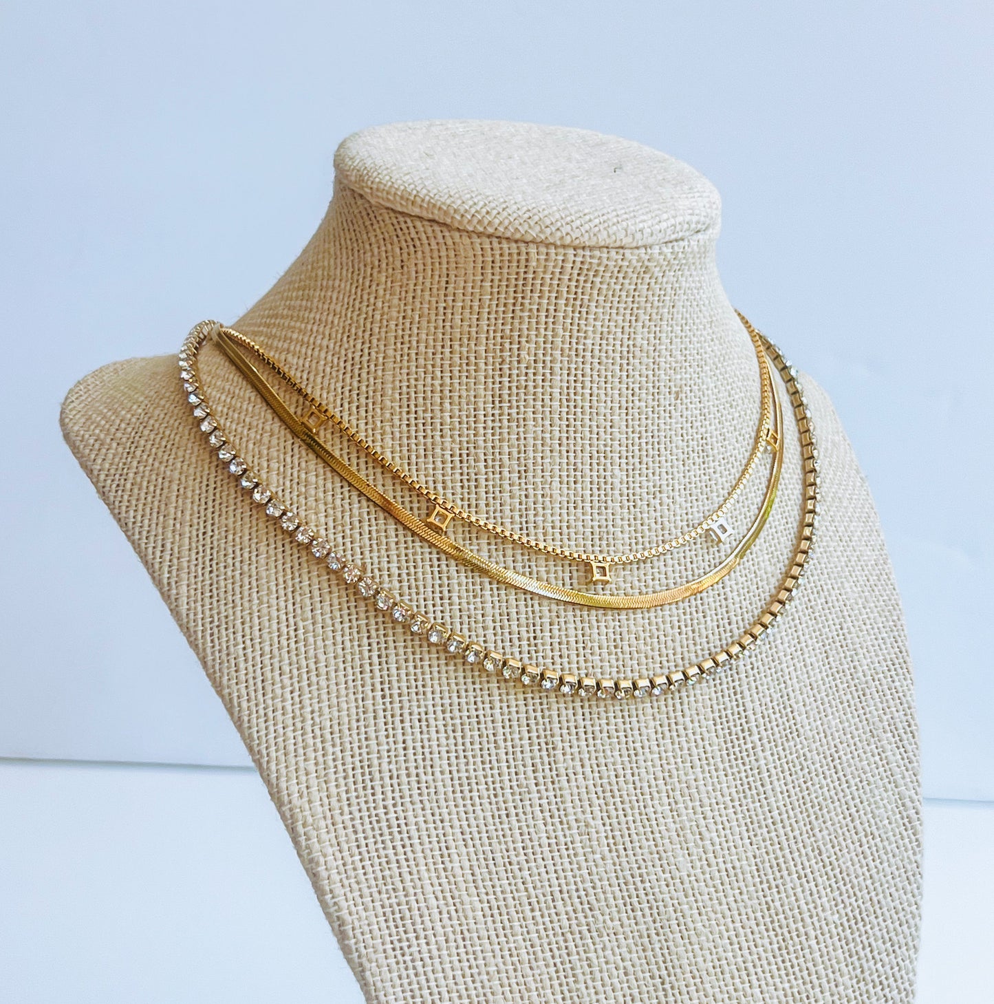 Layered Tennis Necklace Three chain layer gold necklaces on a mannequin bust against a light background