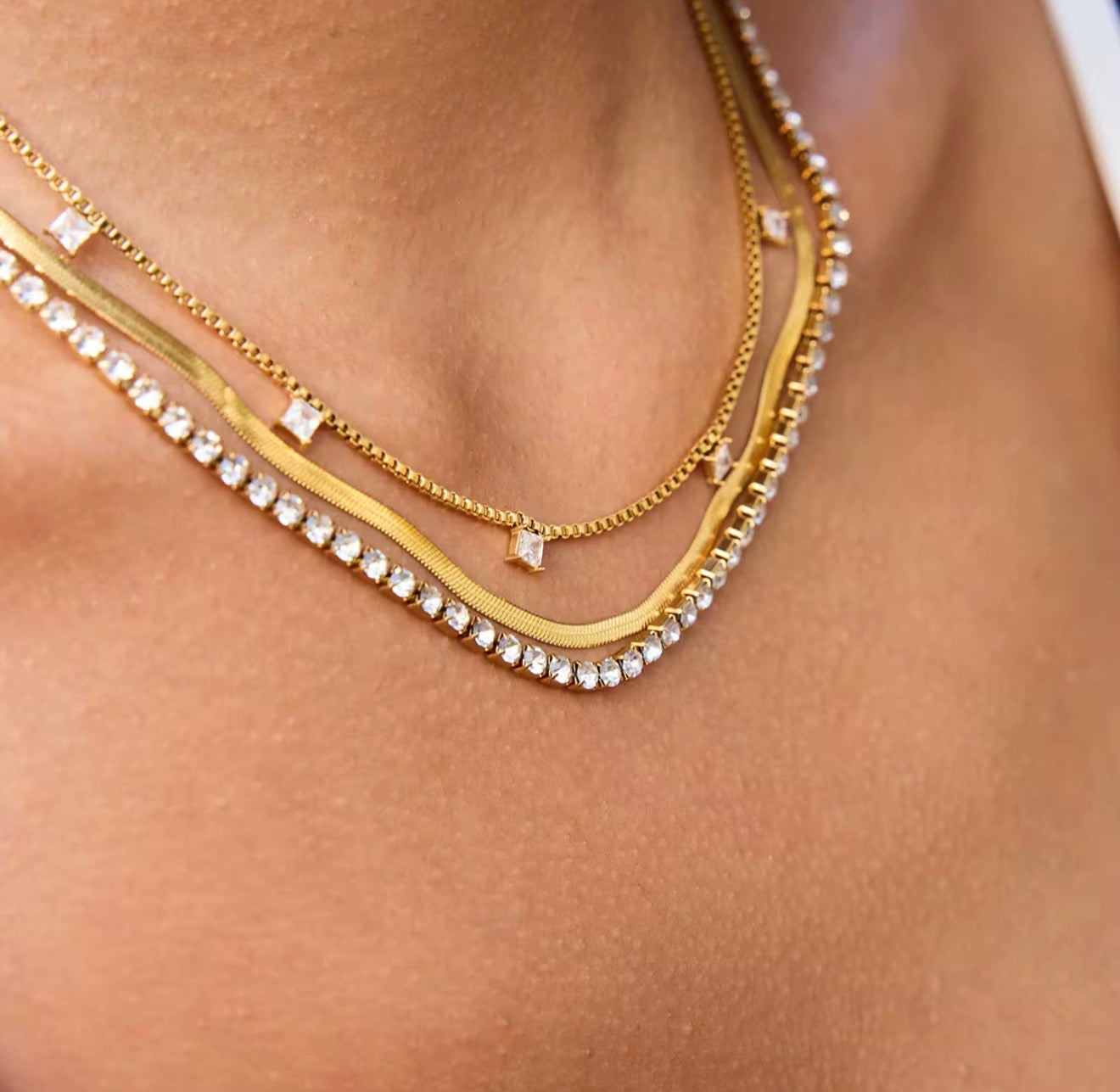 Layered Tennis Necklace Close-up of a person wearing multiple chain layered gold necklace with diamonds 
