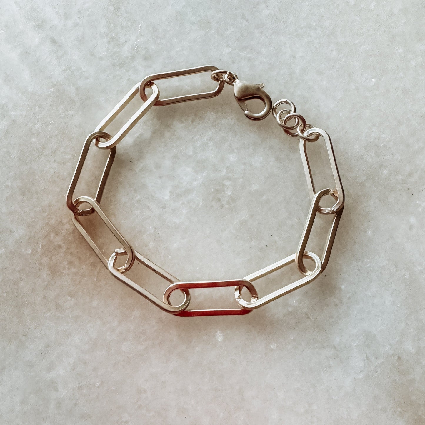 A matte gold bracelet with a paper clip chain design, displayed on a bright background.