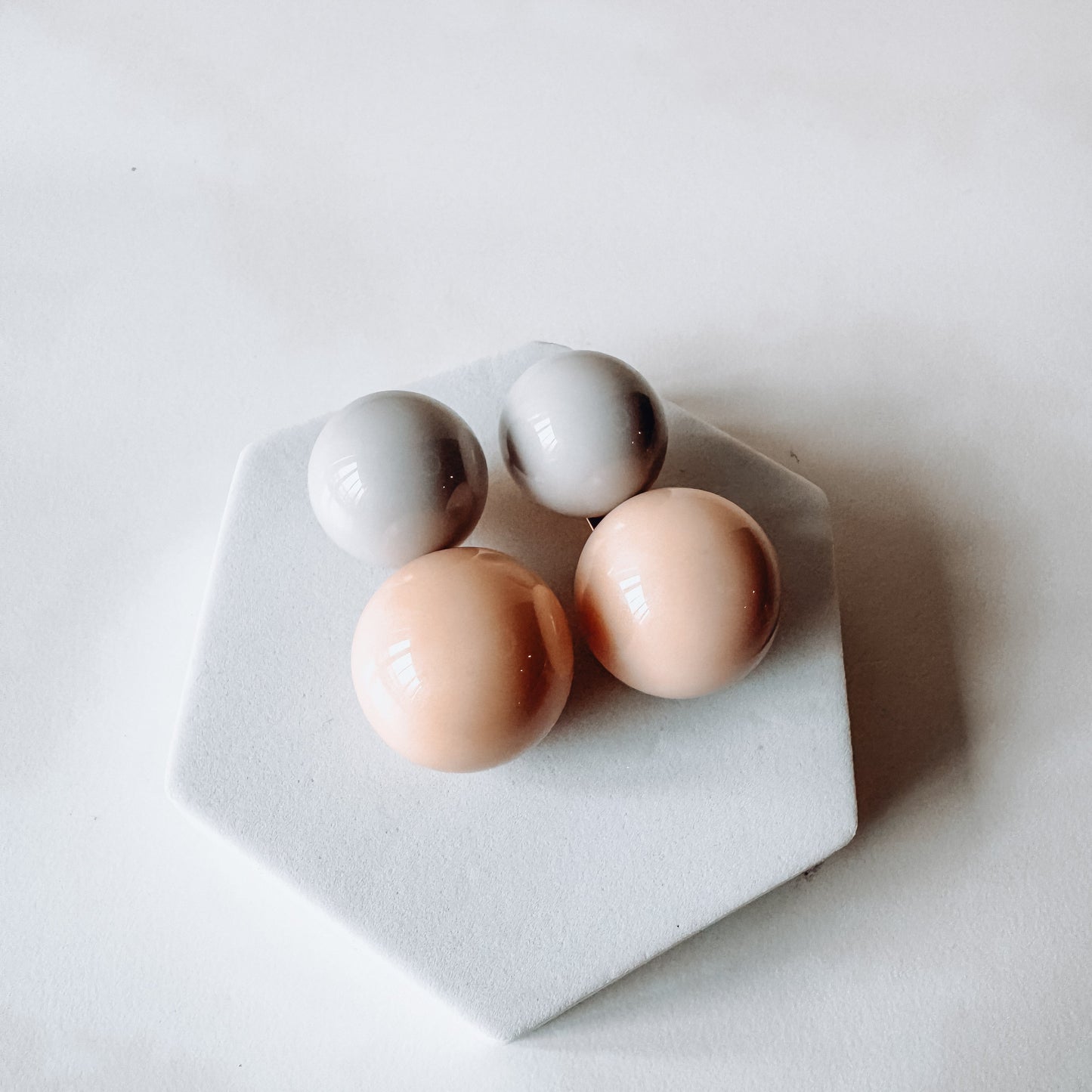 Four round ceramic beads pastel colored earrings on a hexagonal white stand on a white background. 