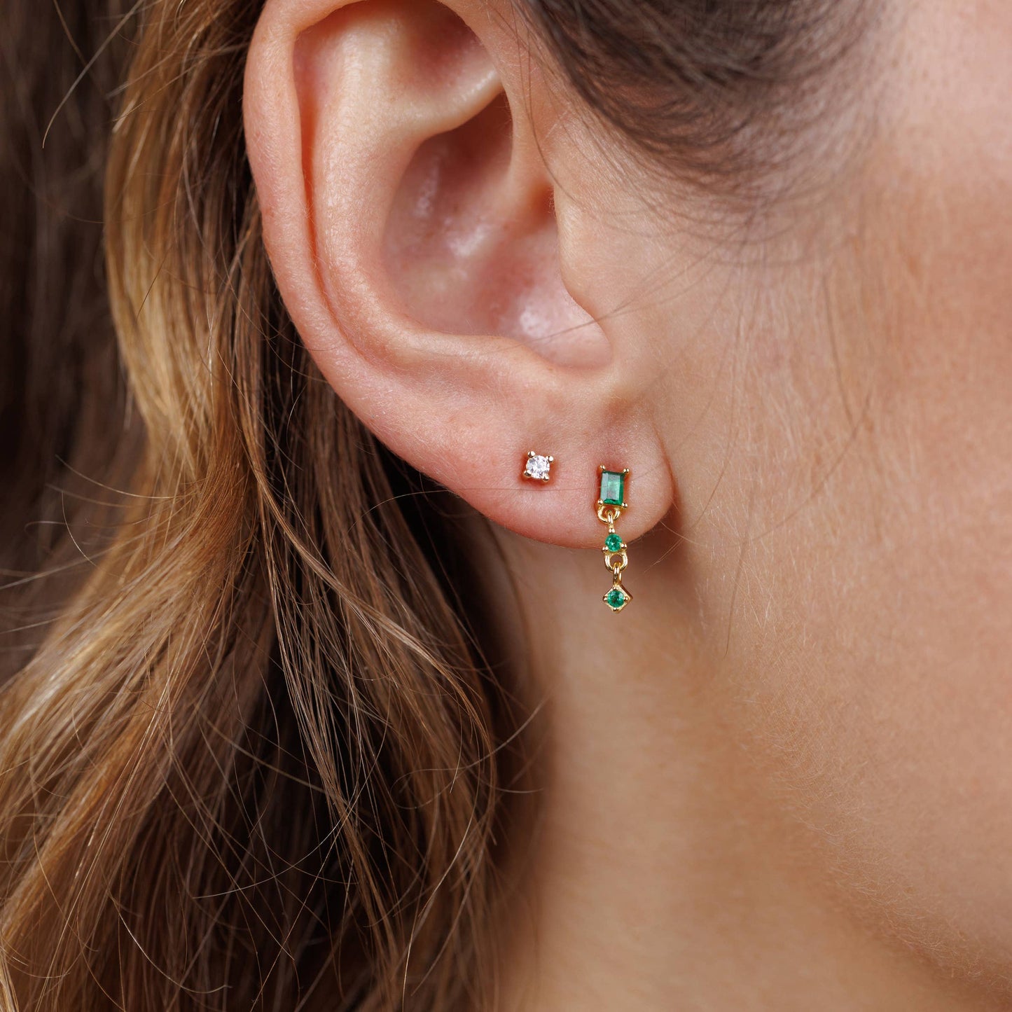 Mini Baguette Drop Earrings - Emerald Close-up of an ear wearing a small earring with a green gems.