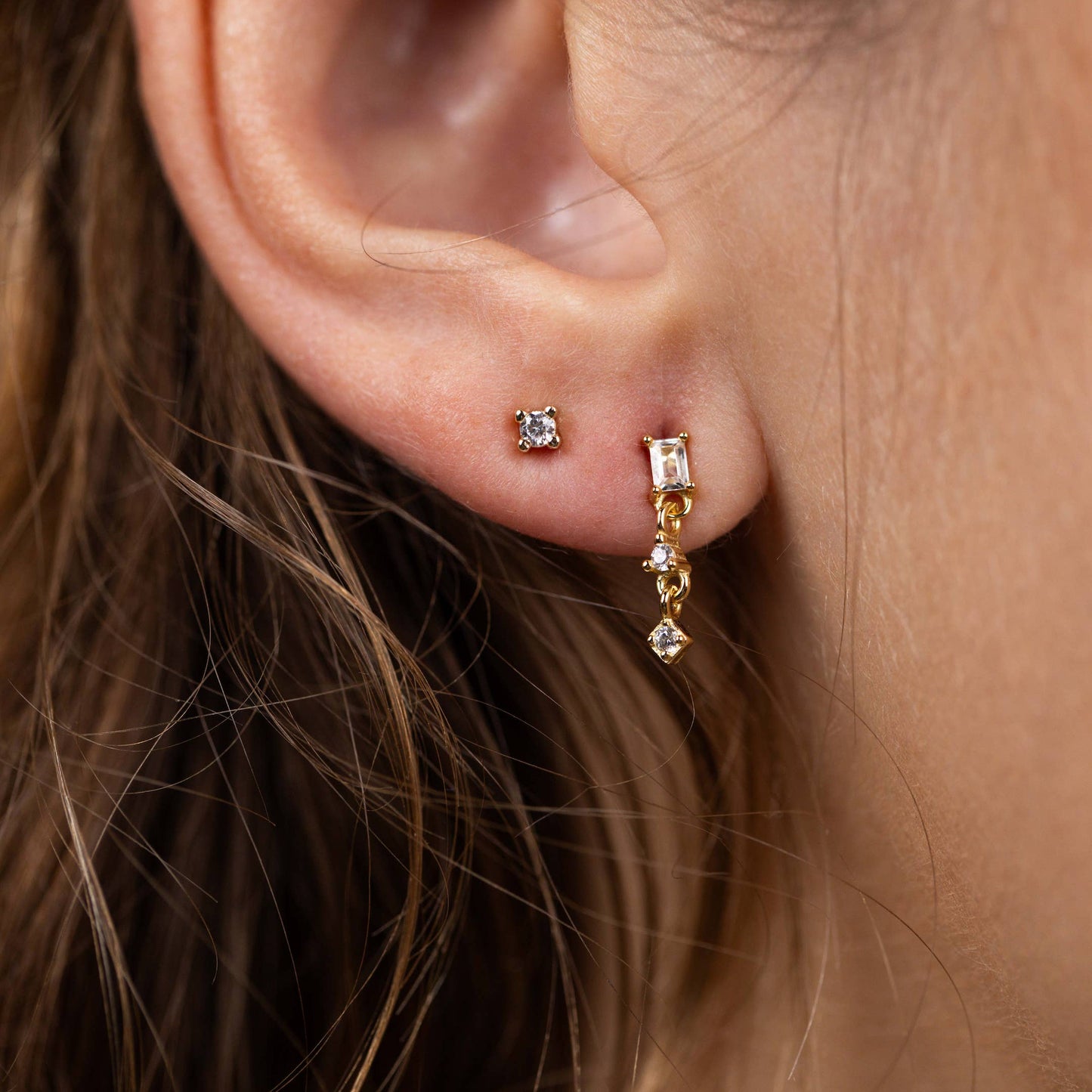 Mini Baguette Drop Earrings - White Close-up of an ear wearing gold on a neutral background