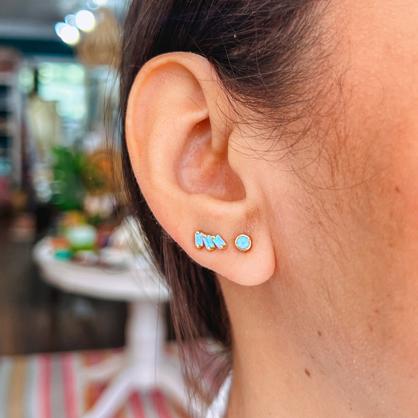 Offset Trio Stud - Fire Opal Close-up of an ear wearing turquoise stud earrings with a blurred background