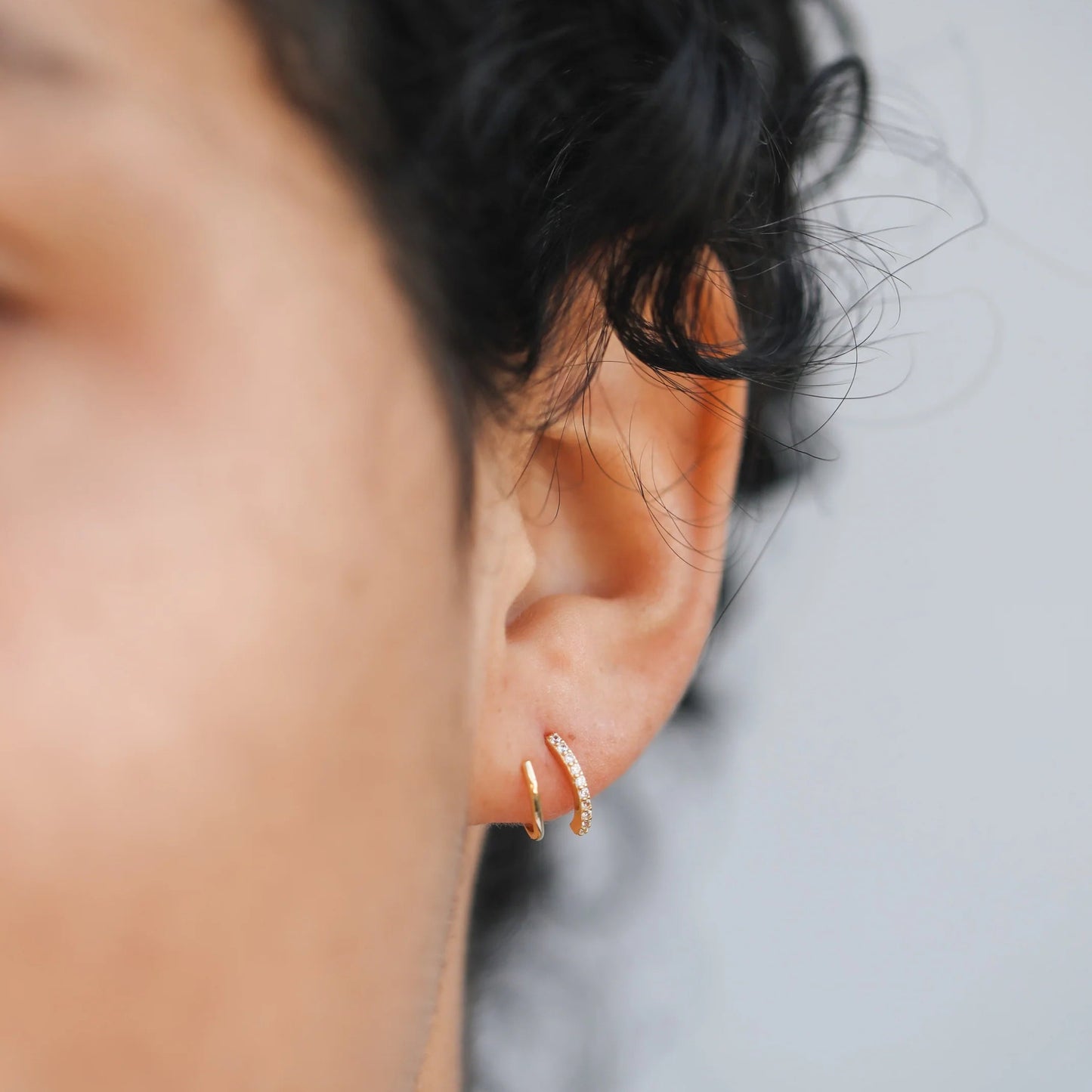 Close-up of an ear wearing a gold earring Pave Spiral Gold Earrings with a blurred background