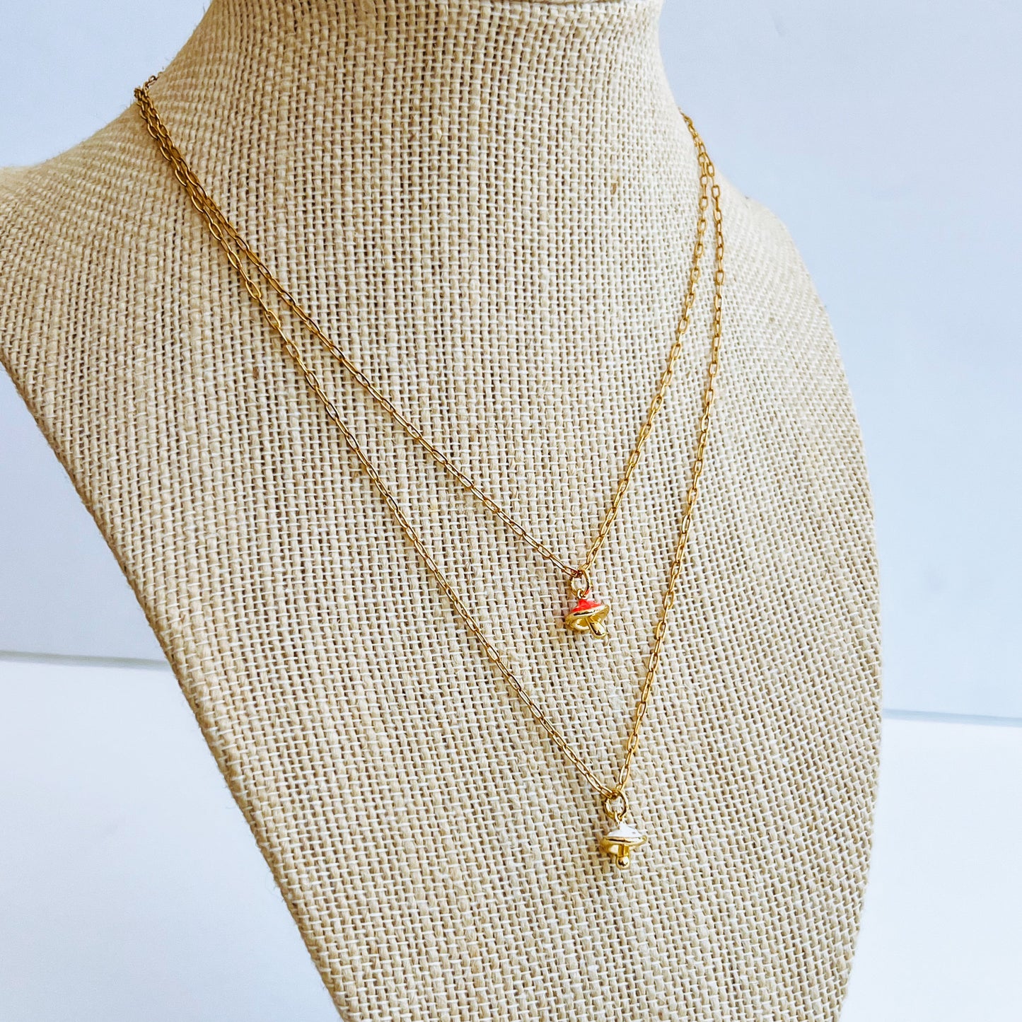 Pink Mushroom Charm Necklace and white charm two Gold necklace with a mushroom pendant on a mannequin bust against a light background