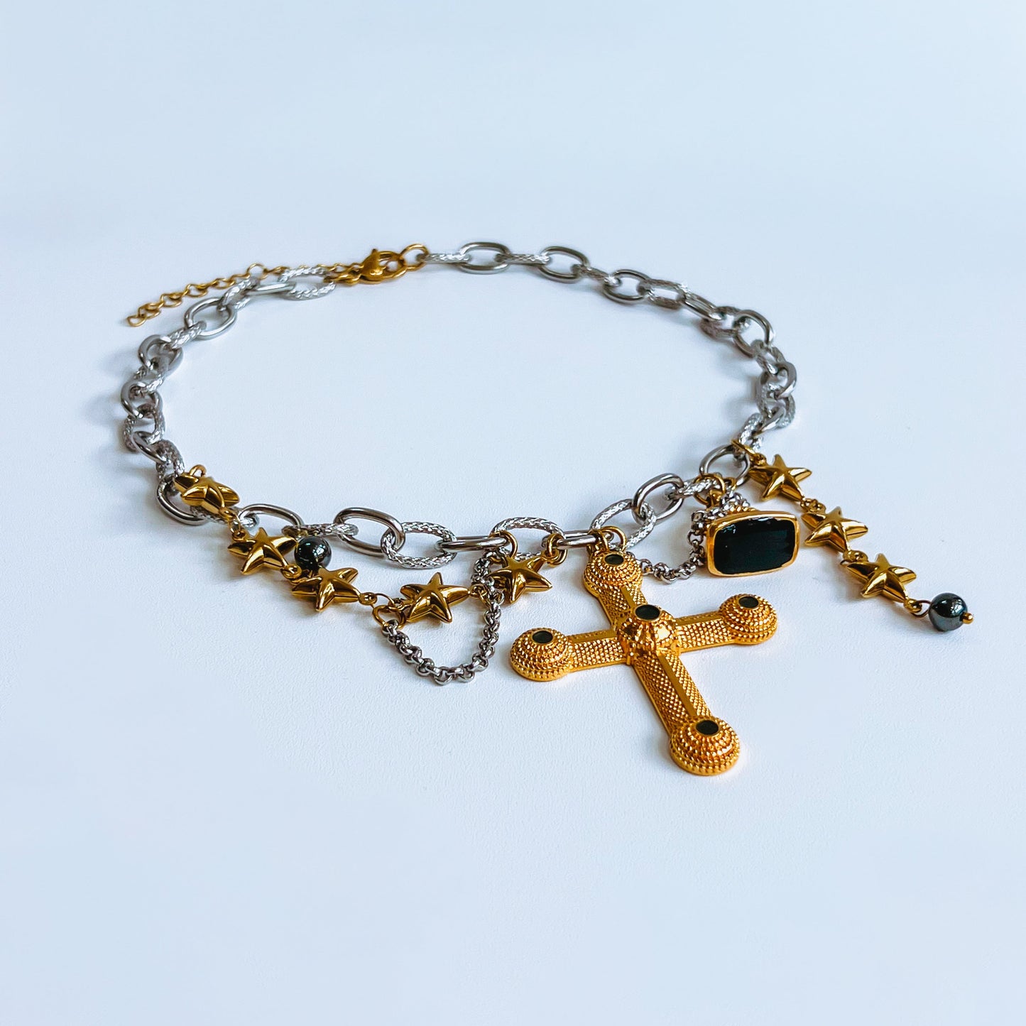 chunky cross necklace with gold cross and star charms on a light blue background