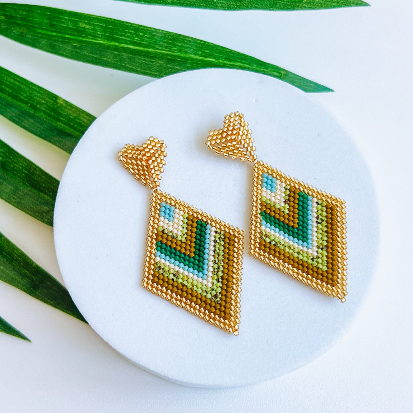 Sienna Beaded Earring Geometric earrings on a round white stand with green leaves in the background