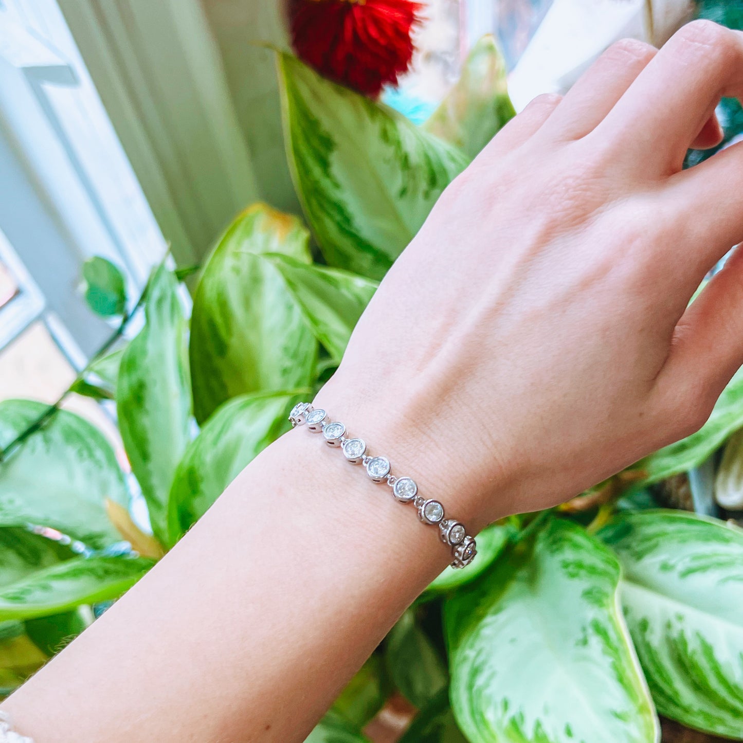Hand wearing a bracelet with green leaves in the background