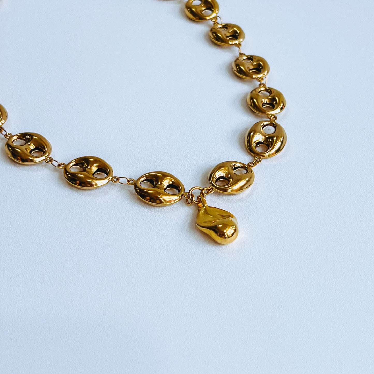 Theta Chunky Necklace - Gold closeup Gold necklace with gold pendants on a light background