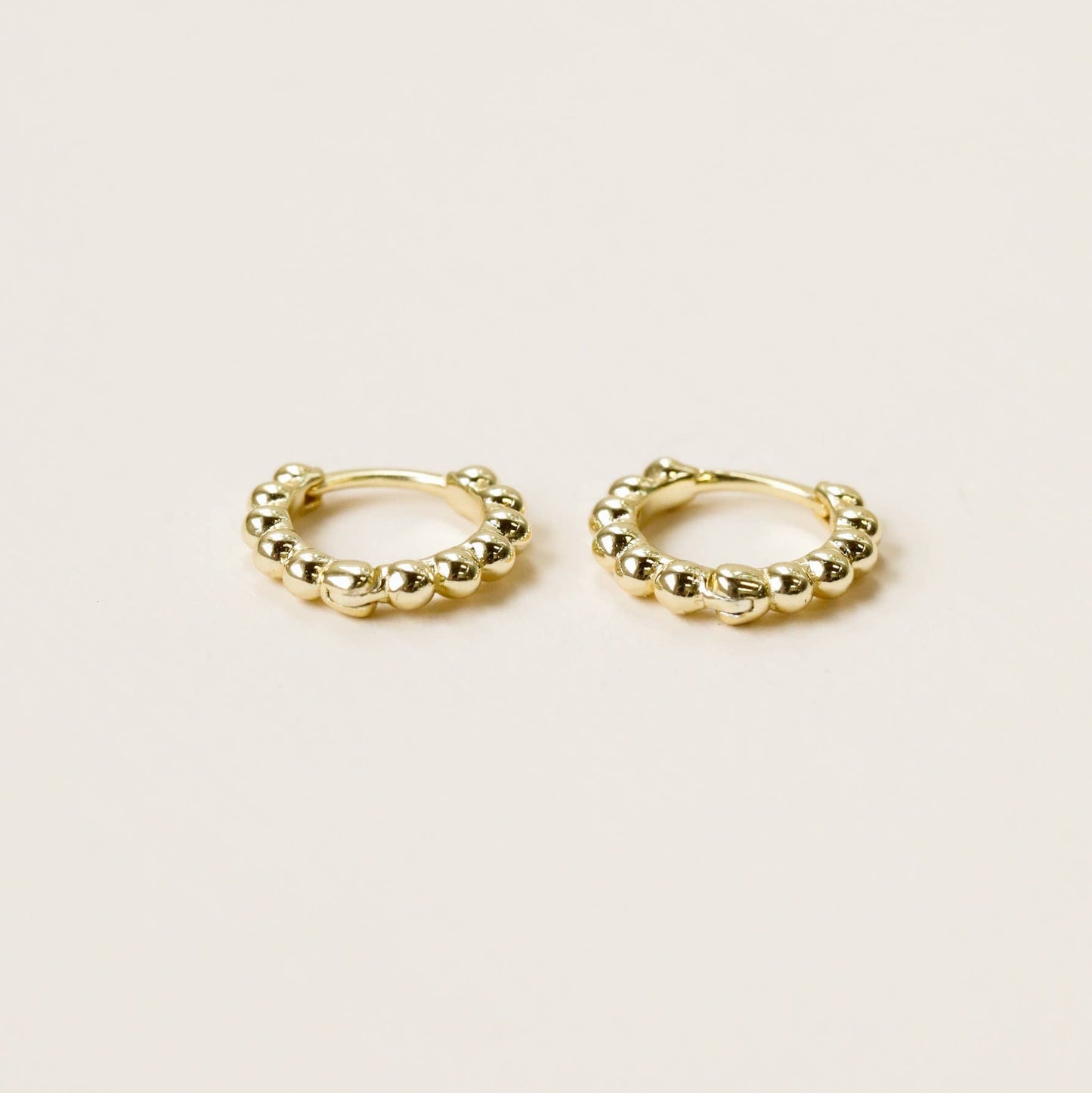 Tiny Gold Earrings - Ball Hoop Pair of gold hoop earrings laid on side