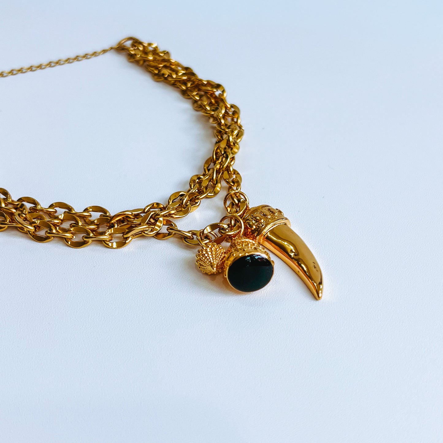 Gold triple layered chain necklace with a unique pendant on a light blue background