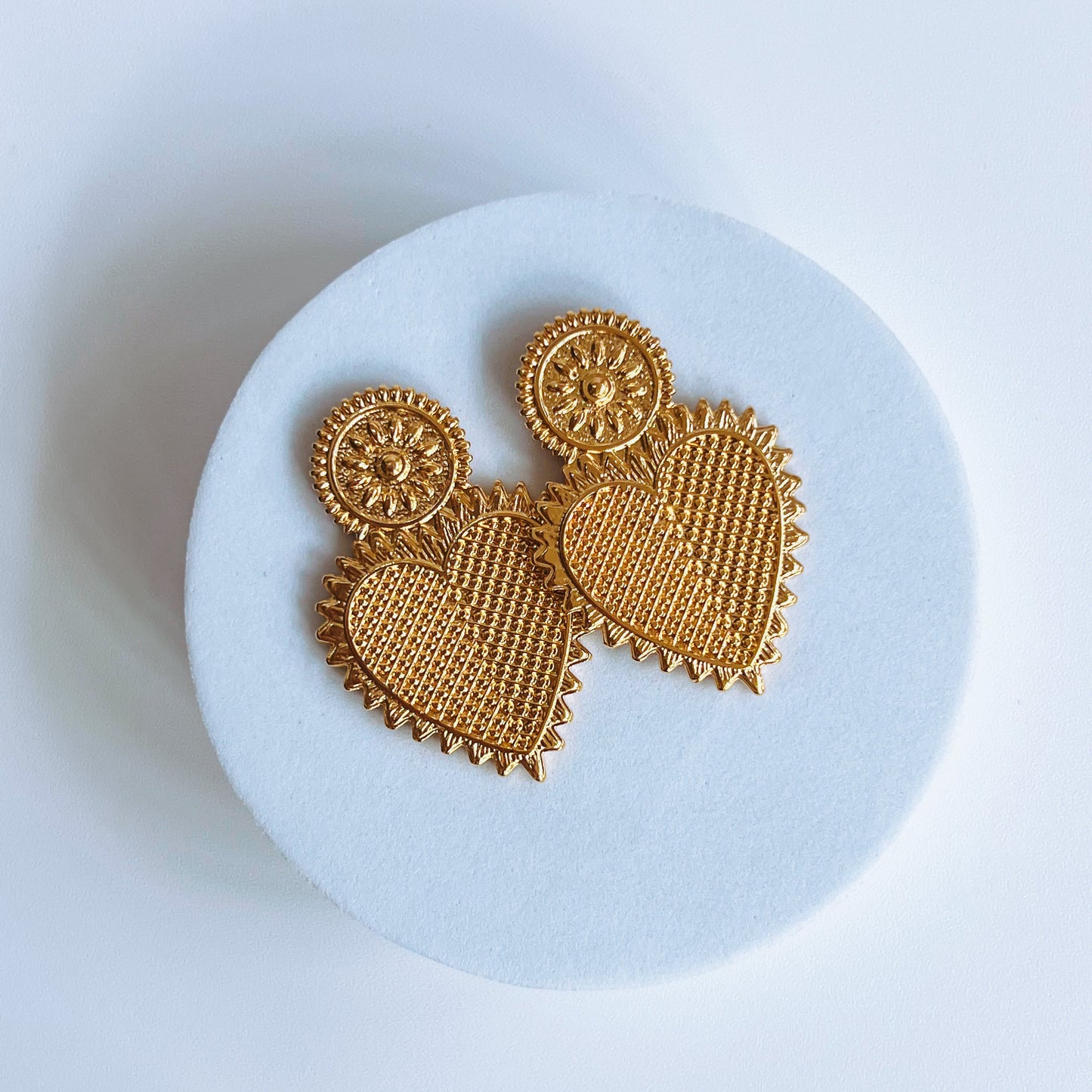 Vintage Heart Earrings - Gold earrings on a white round stand with a white background