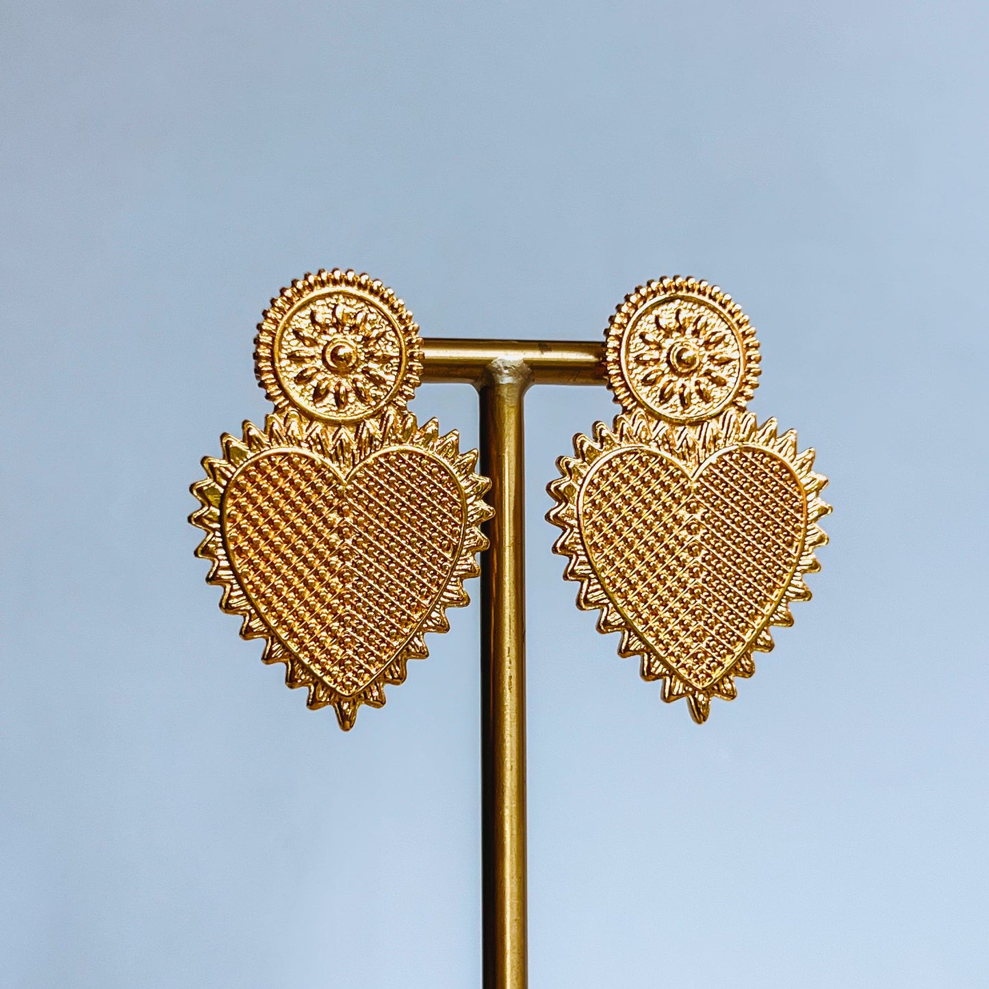 Vintage Heart Earrings - Gold heart-shaped earrings on a stand against a light blue background