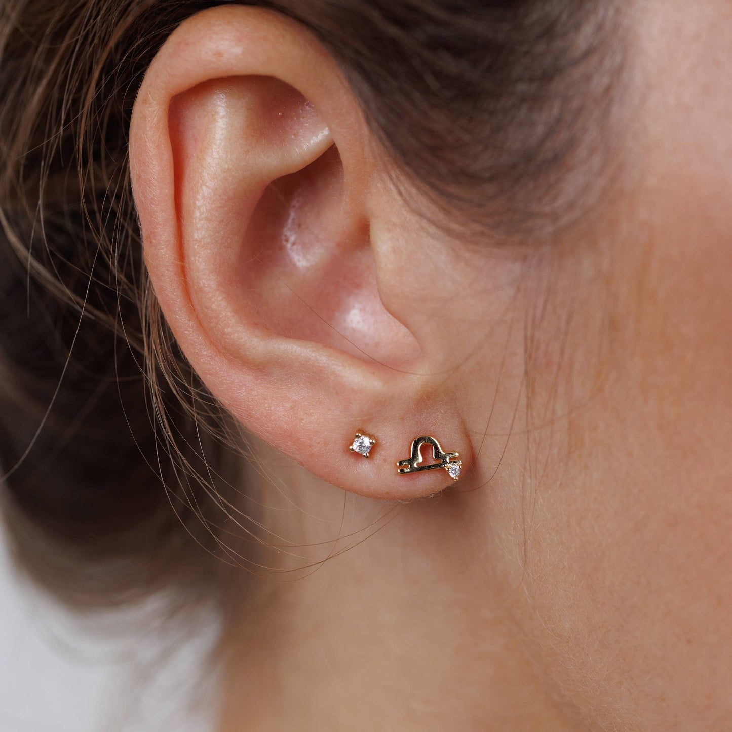 Zodiac Gold Earrings - Libra Close-up of an ear wearing a small gold earring.
