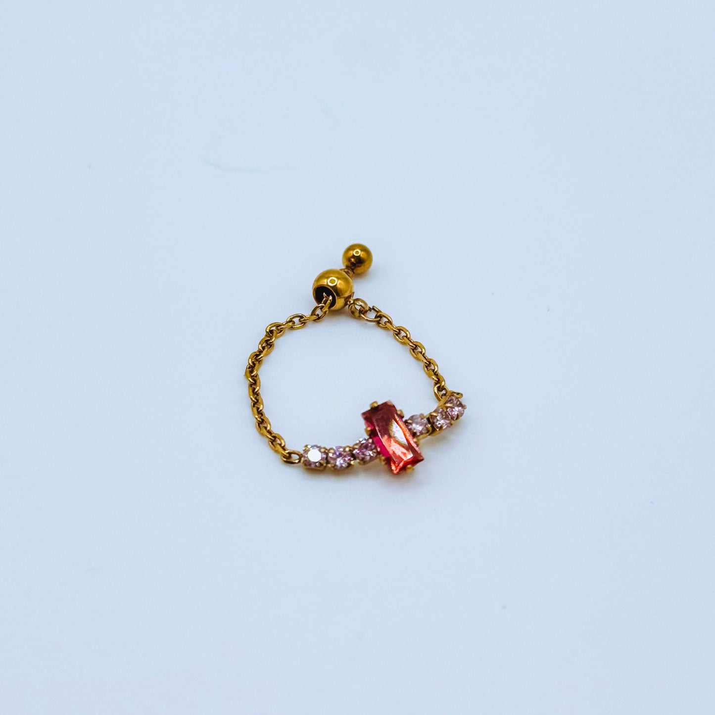 Gold chain ring with a pink gemstone on a light background