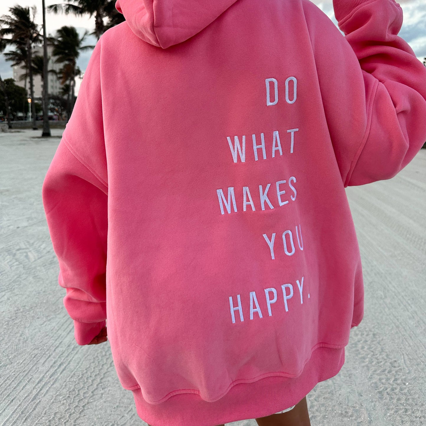 Person wearing a pink hoodie with a motivational quote on the beach