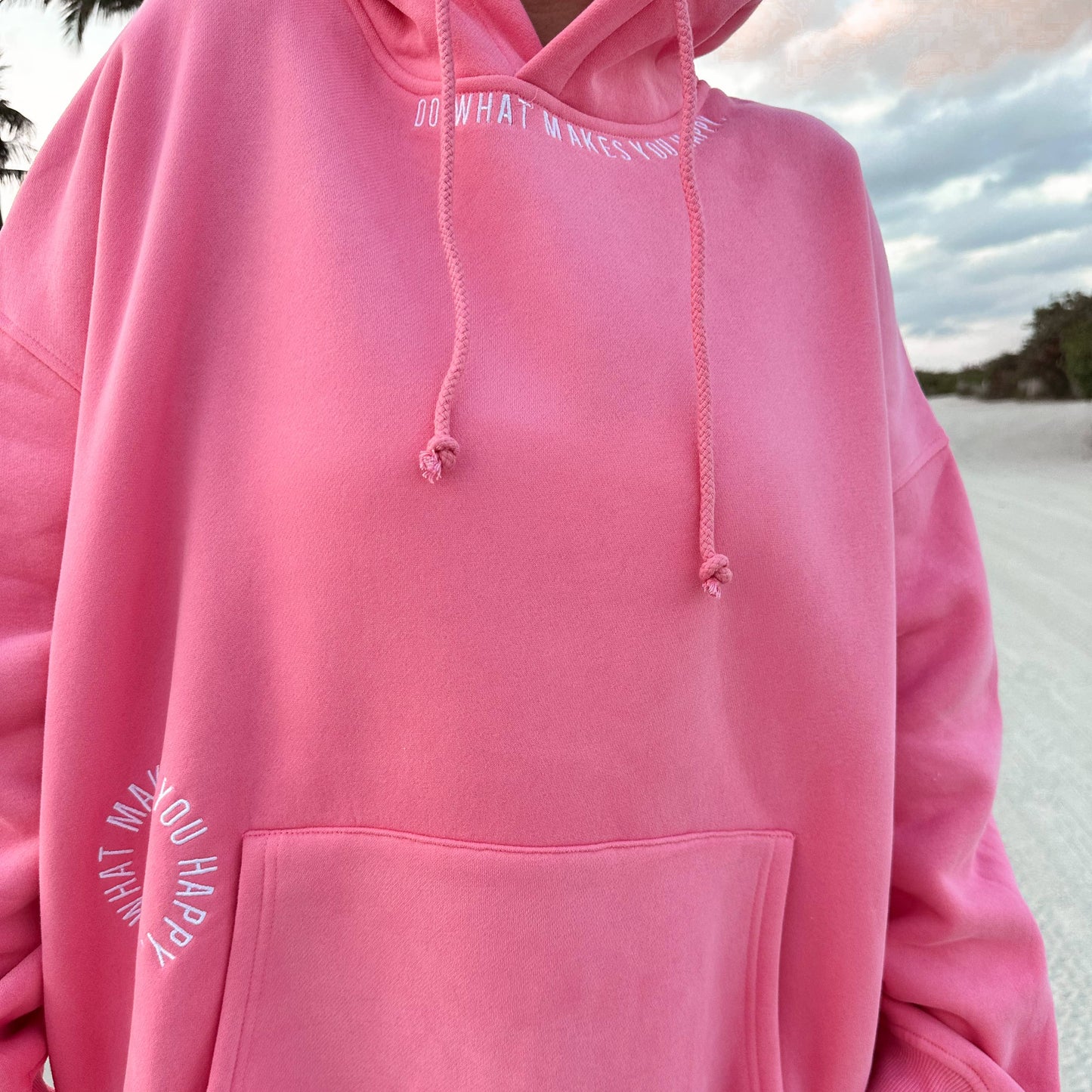 Do What Makes You Happy Embroidered Hoodie - Pink Person wearing a pink hoodie with text on it, standing outdoors.