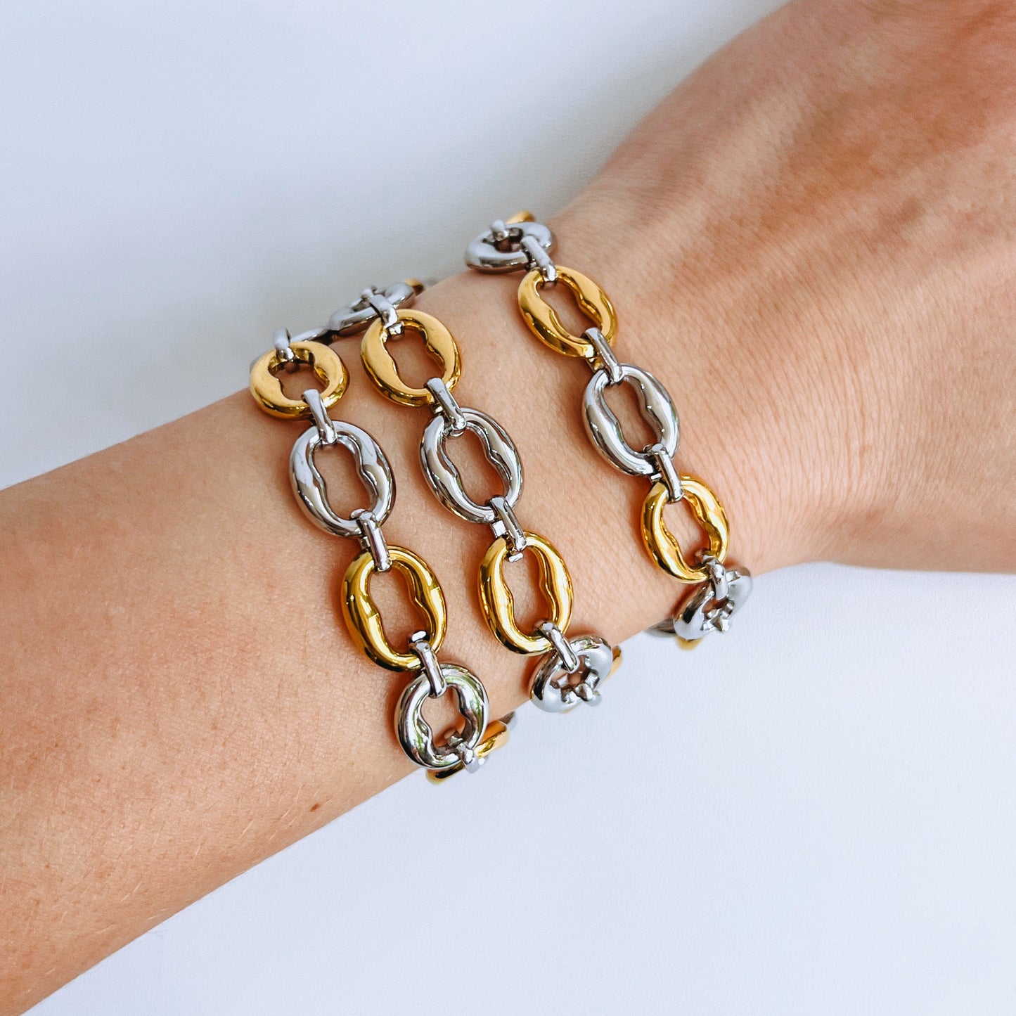 three mixed metal link chain bracelets on a wrist against a white background