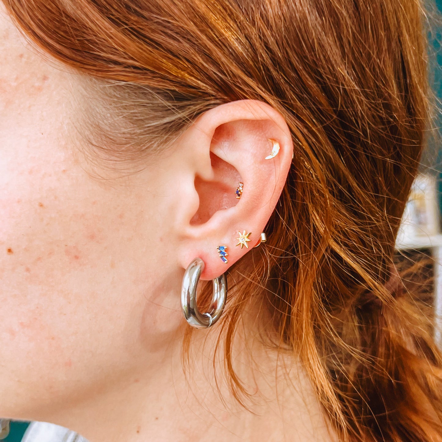Close-up of an ear featuring silver  stainless steel hoop ring earring with multiple earrings against a blurred background