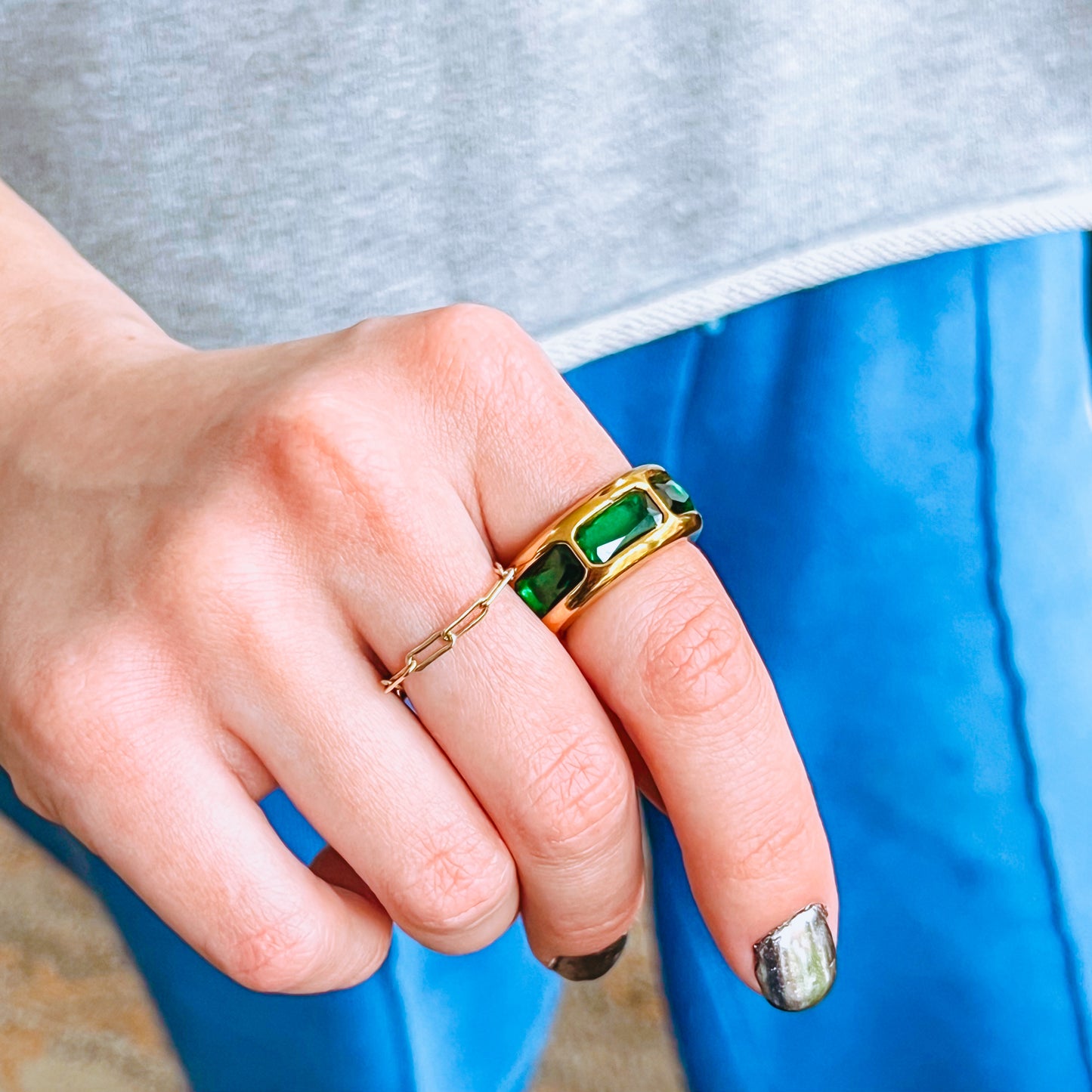 Hand wearing a vintage style gold ring with green gemstones against a blurred background